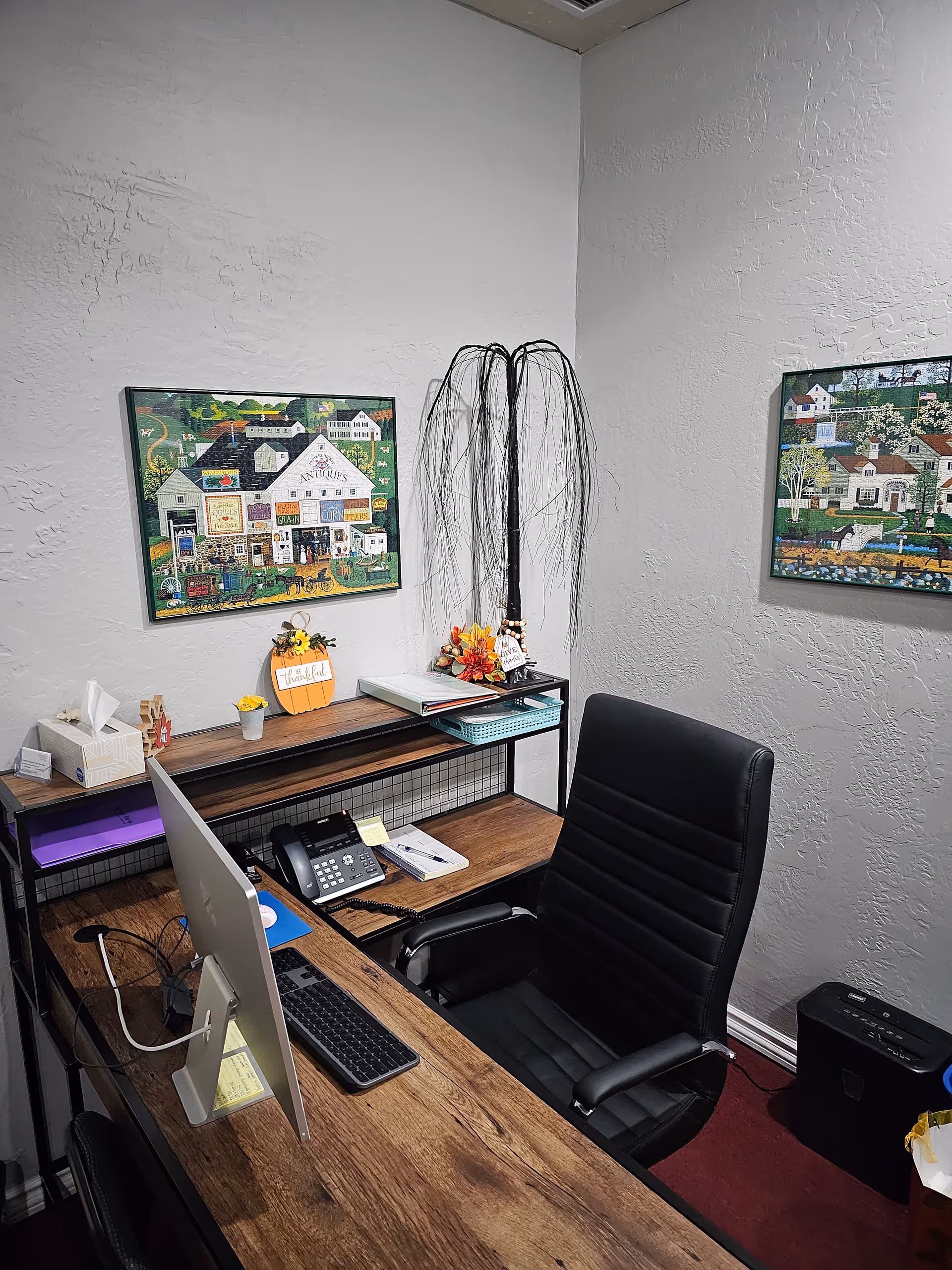 Office corner with desk, computer, phone, chair, and wall art in a senior living facility.