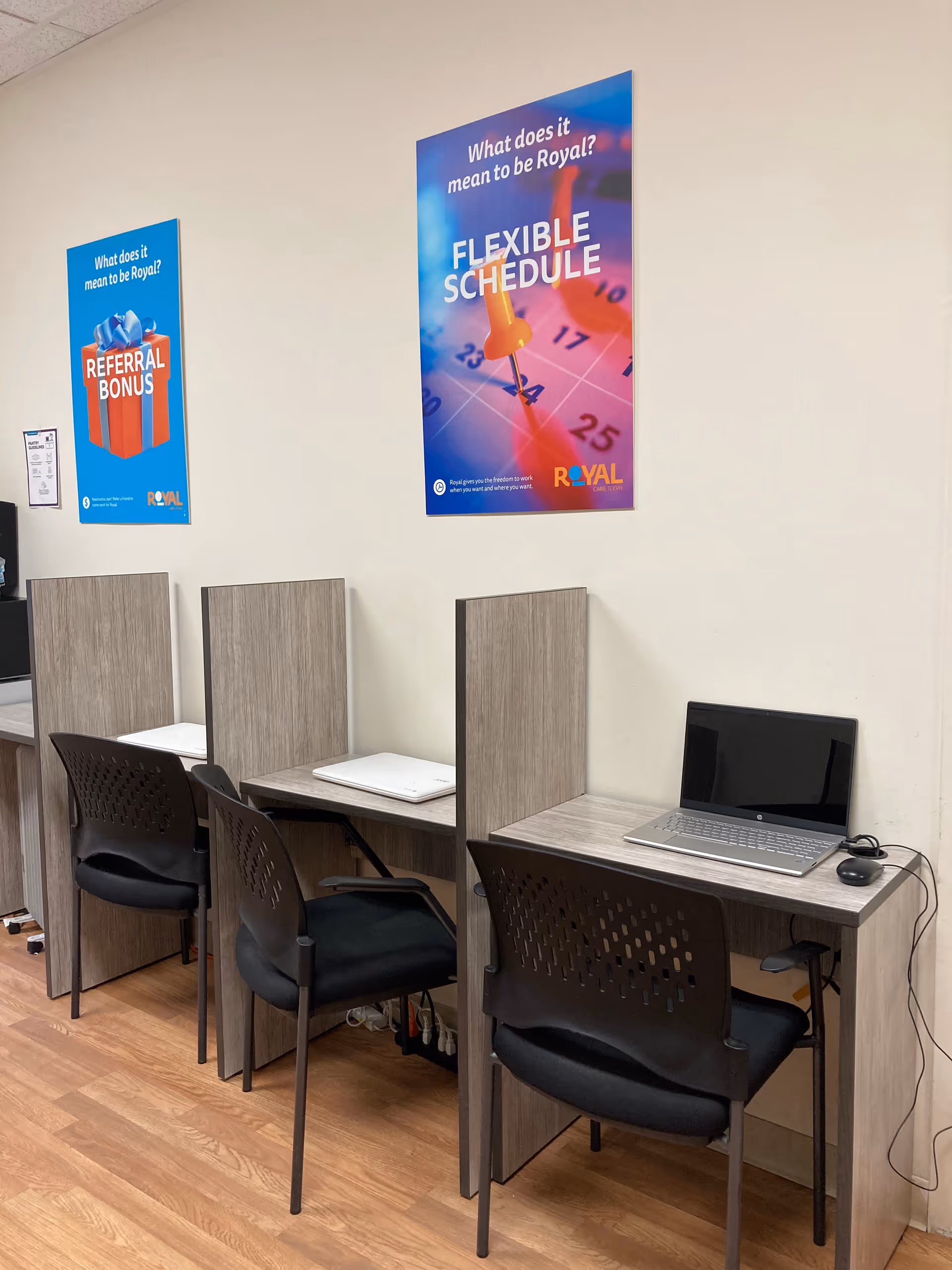 Row of study desks separated by partitions with a laptop and chairs, posters on the wall.