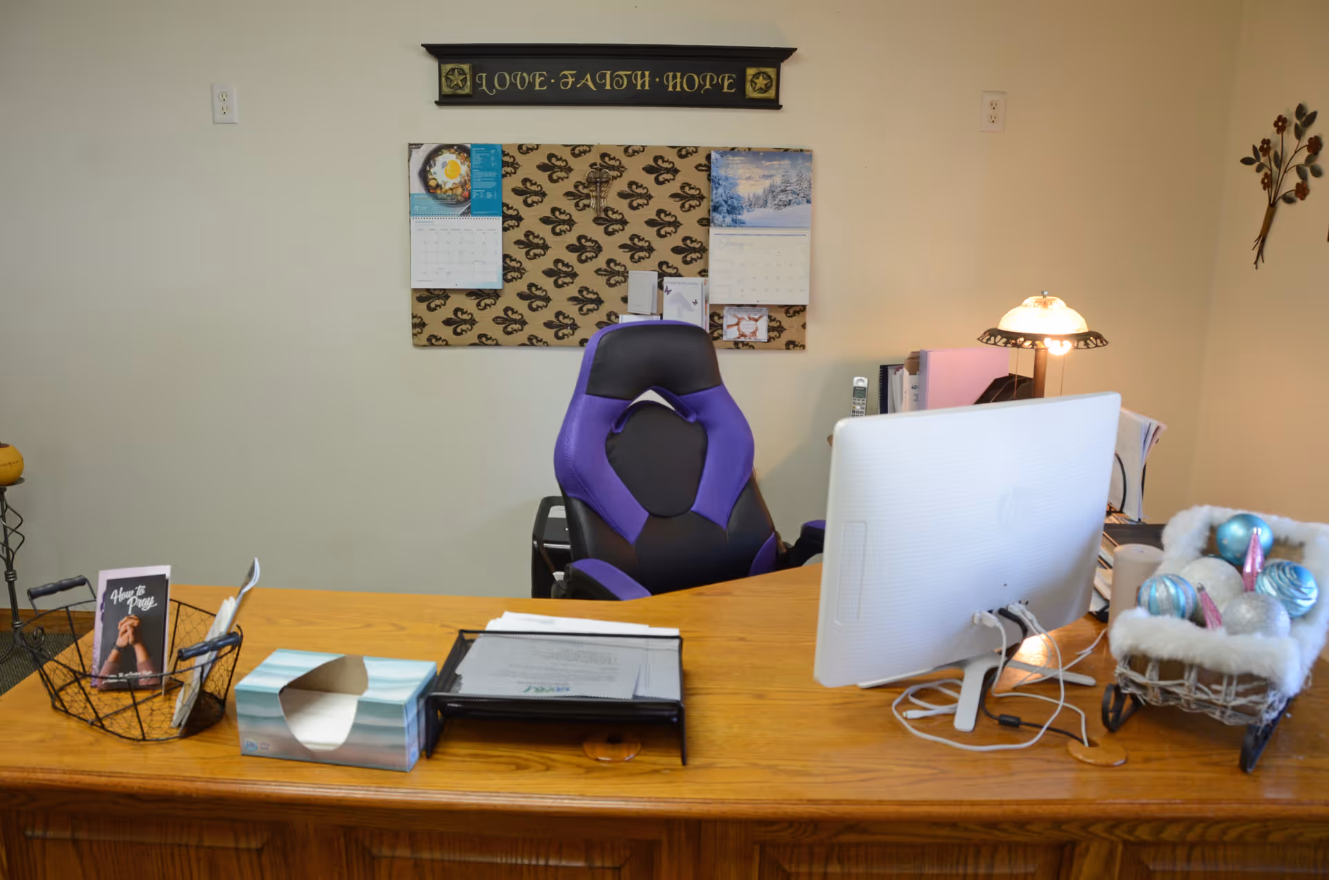 Office desk with computer, purple chair, calendar, lamp, and decorative items.
