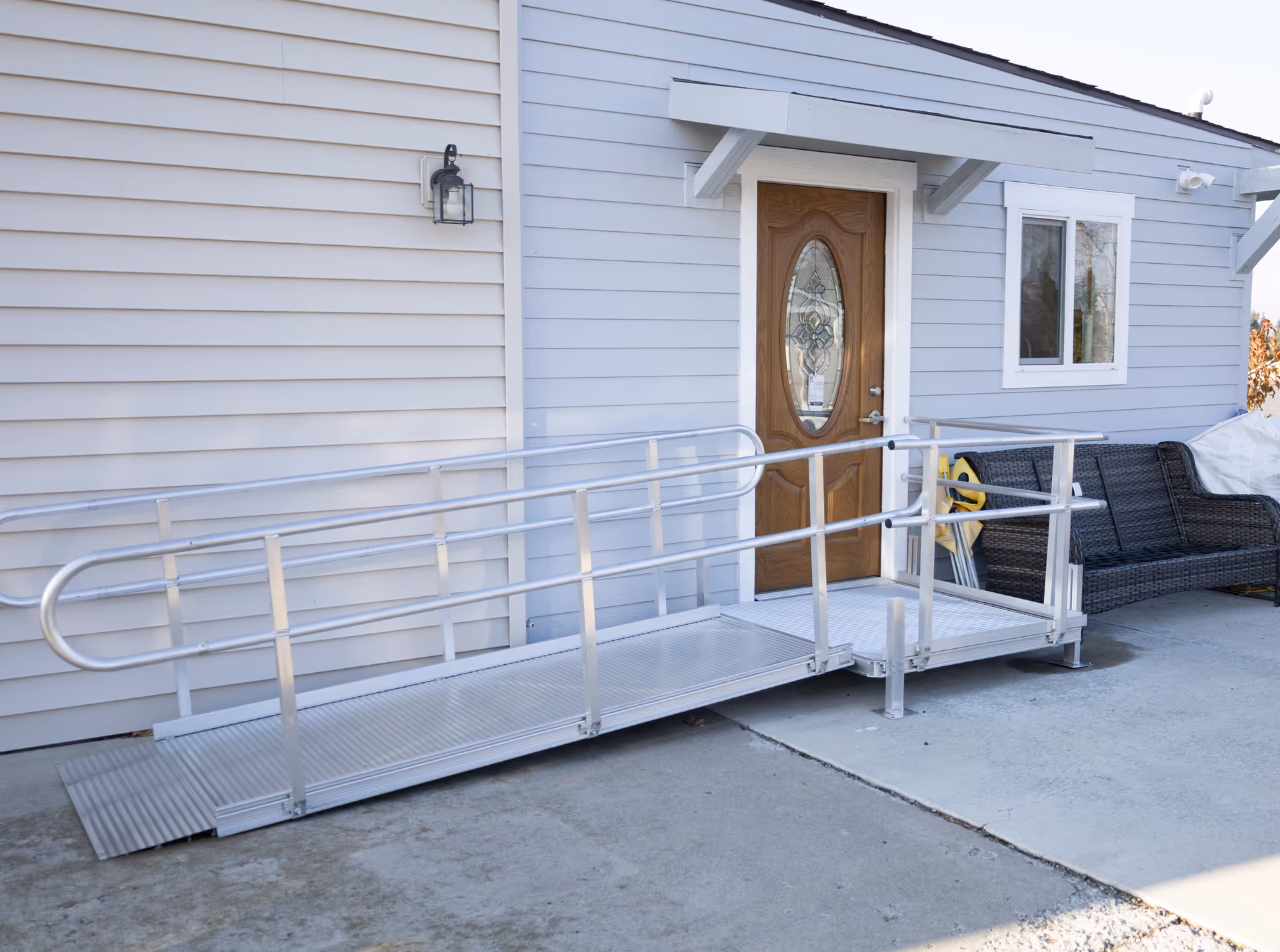 Exterior entrance of a senior facility with a metal accessibility ramp and outdoor seating.