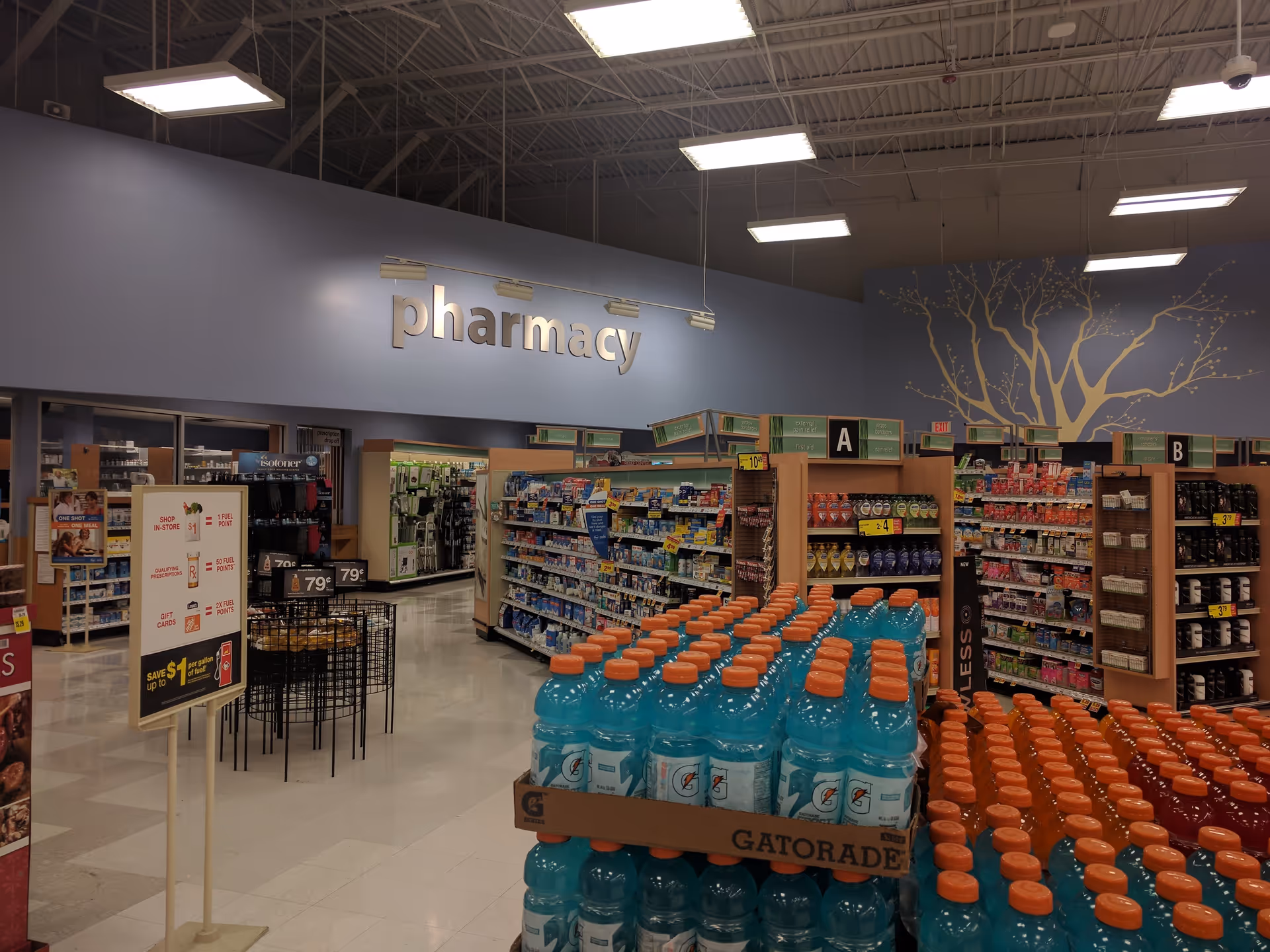 Interior of a Kroger Pharmacy area with aisles, shelves, and large bottled drinks in foreground.