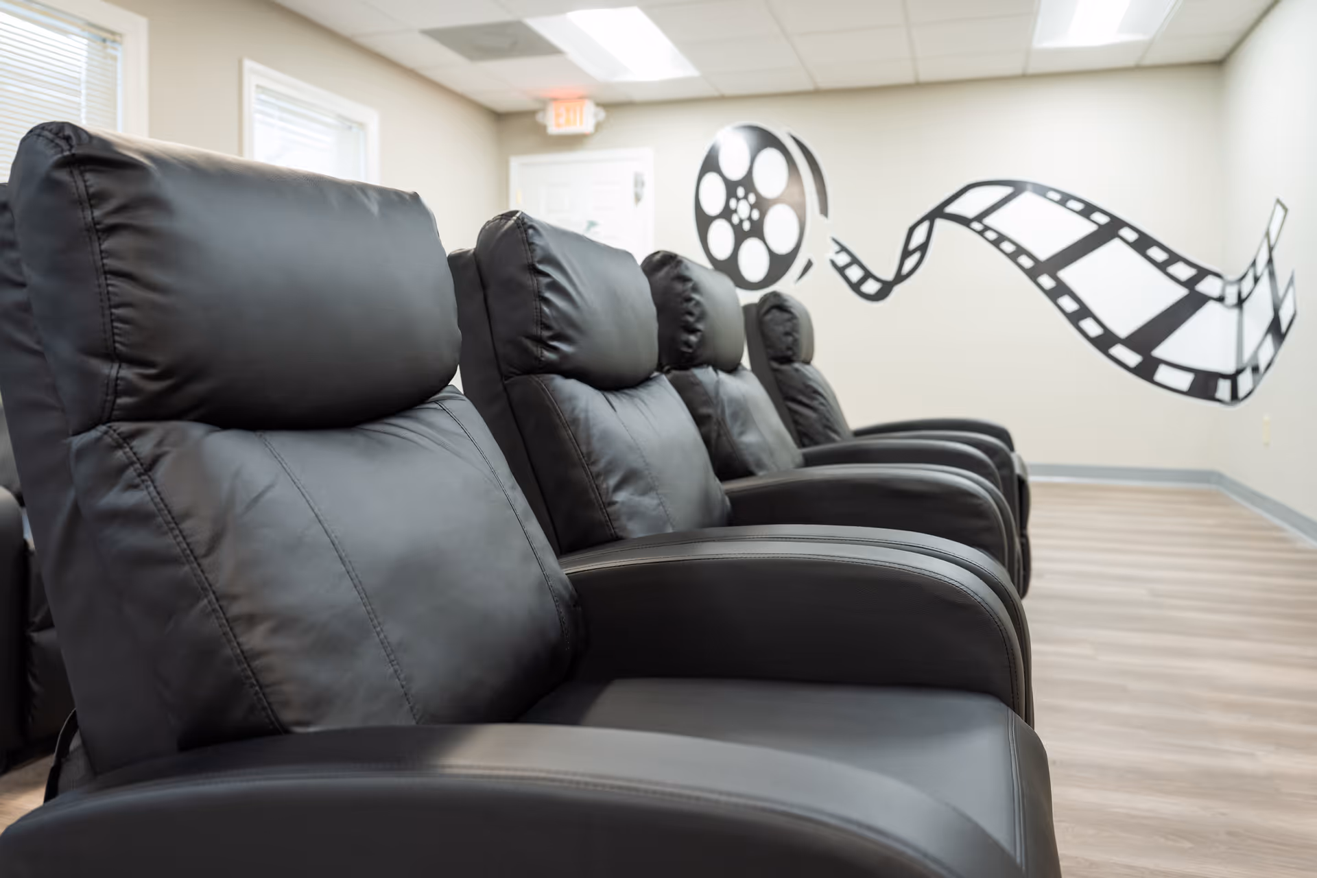 Row of black leather recliners in a modern lounge with film mural.