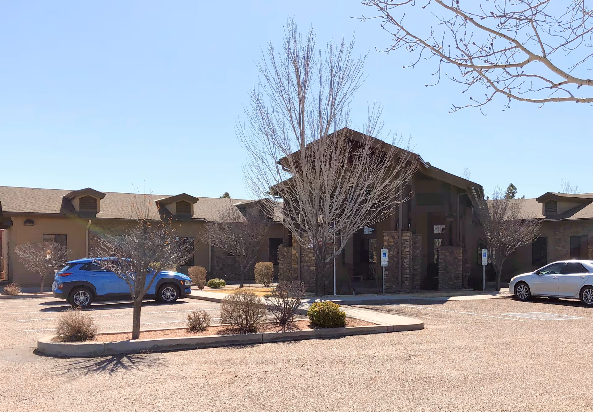 A single-story senior living facility exterior with a stone entrance and parking lot.