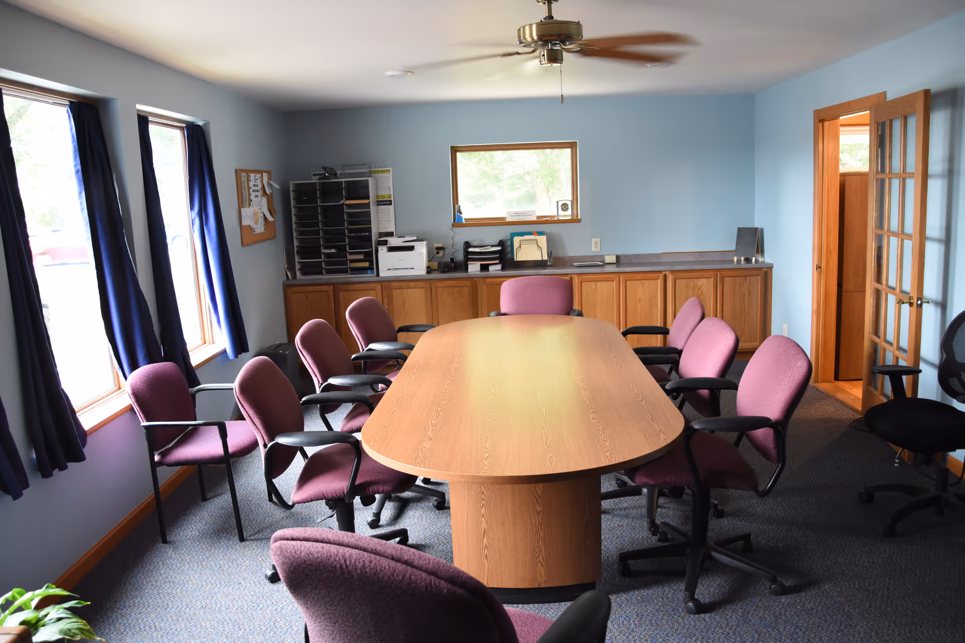 A conference room with a long wooden table and purple chairs.