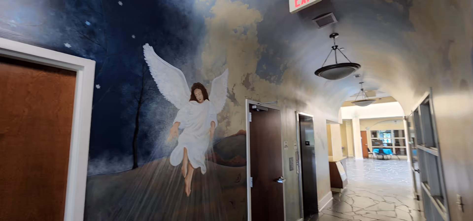 Long hallway inside a facility with an angel mural on an arched ceiling.