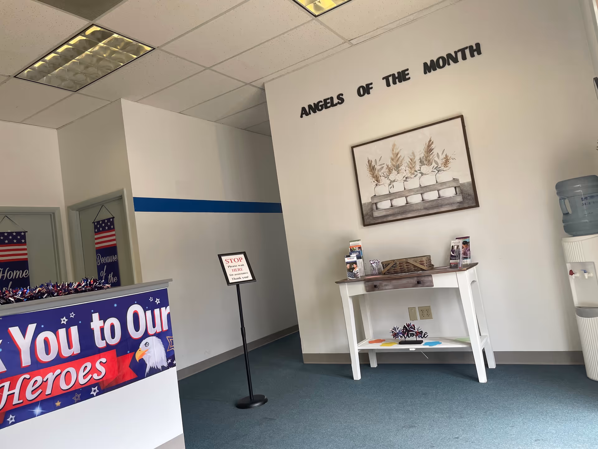 Interior reception area featuring 'Angels Of The Month' display and patriotic decor.