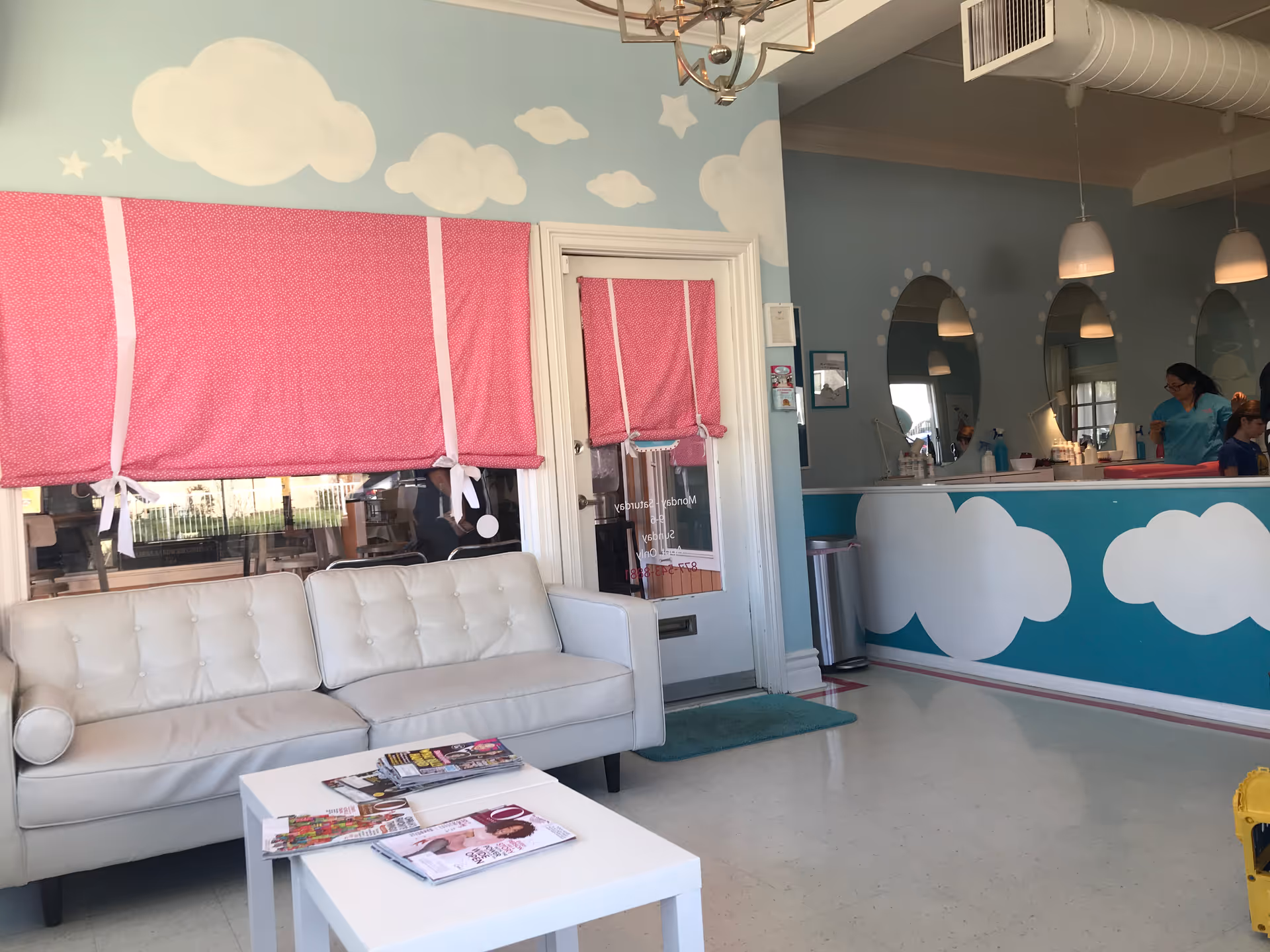 Bright pastel lobby with white sofas, pink blinds, cloud murals, and a reception desk.