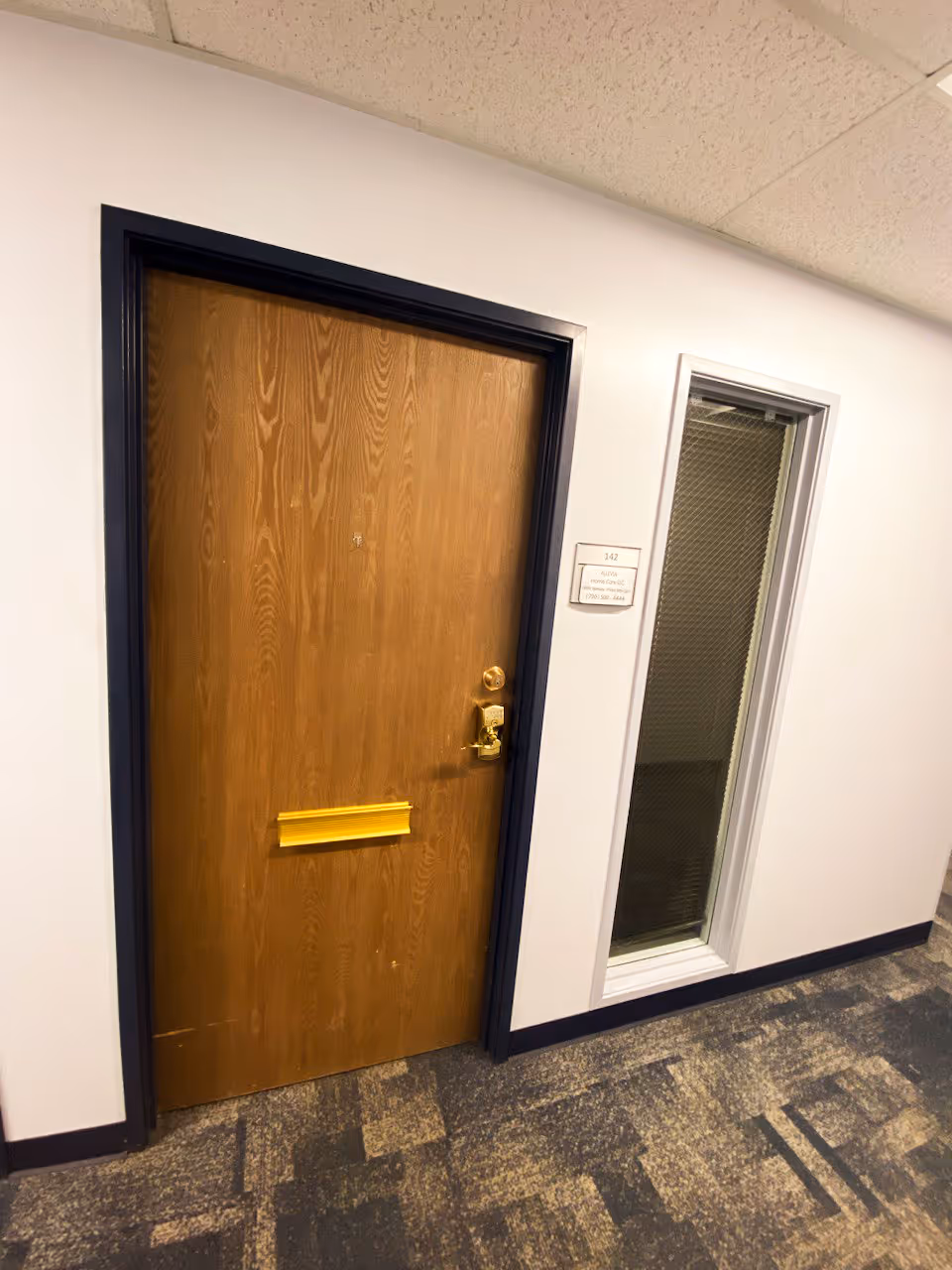 Wooden door in a hallway with a small window and carpeted floor.