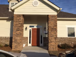 Exterior view of a senior living facility entrance with stone columns and a red door.