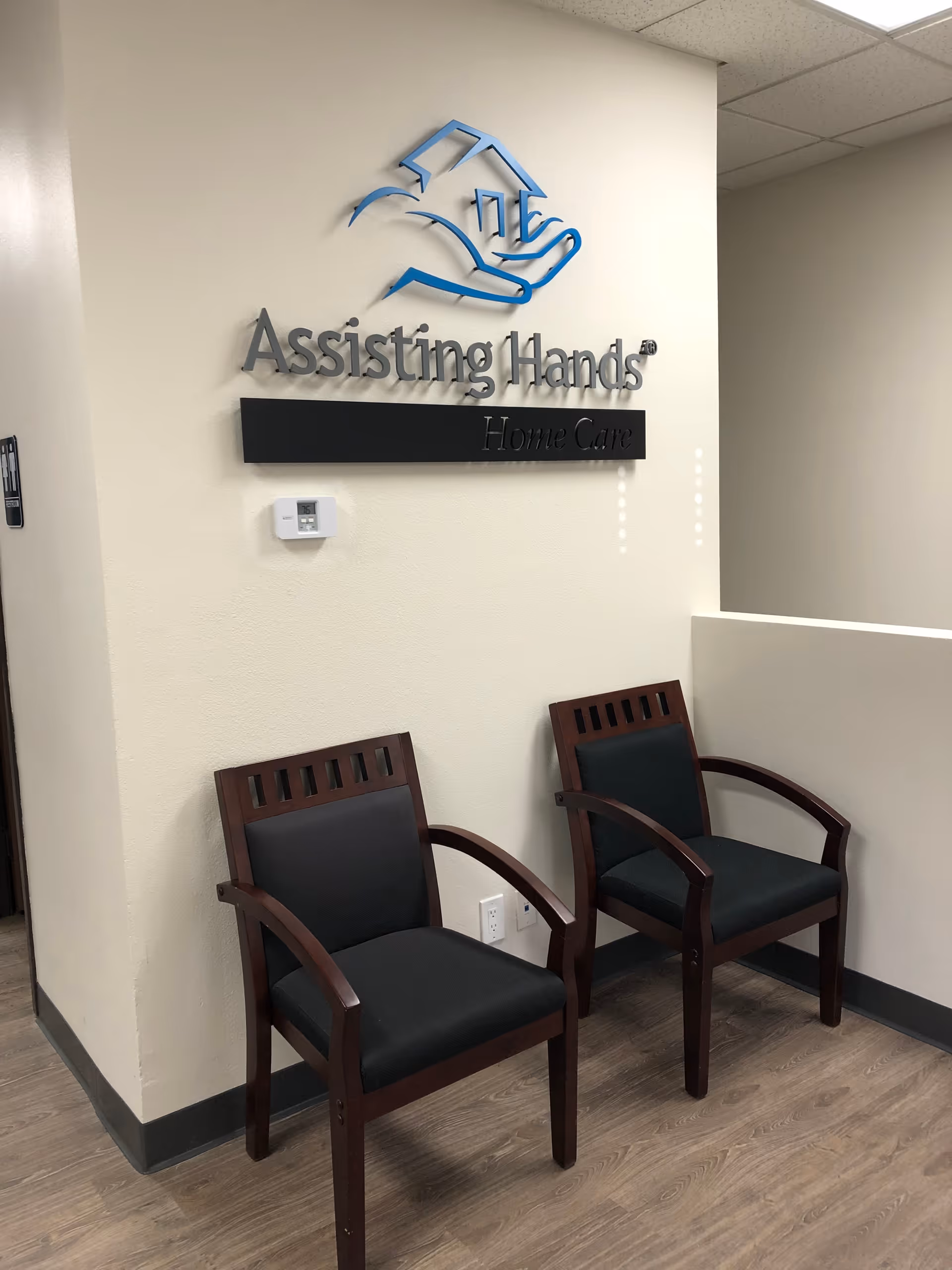 Reception area with two wooden chairs and a wall sign reading Assisting Hands Home Care.