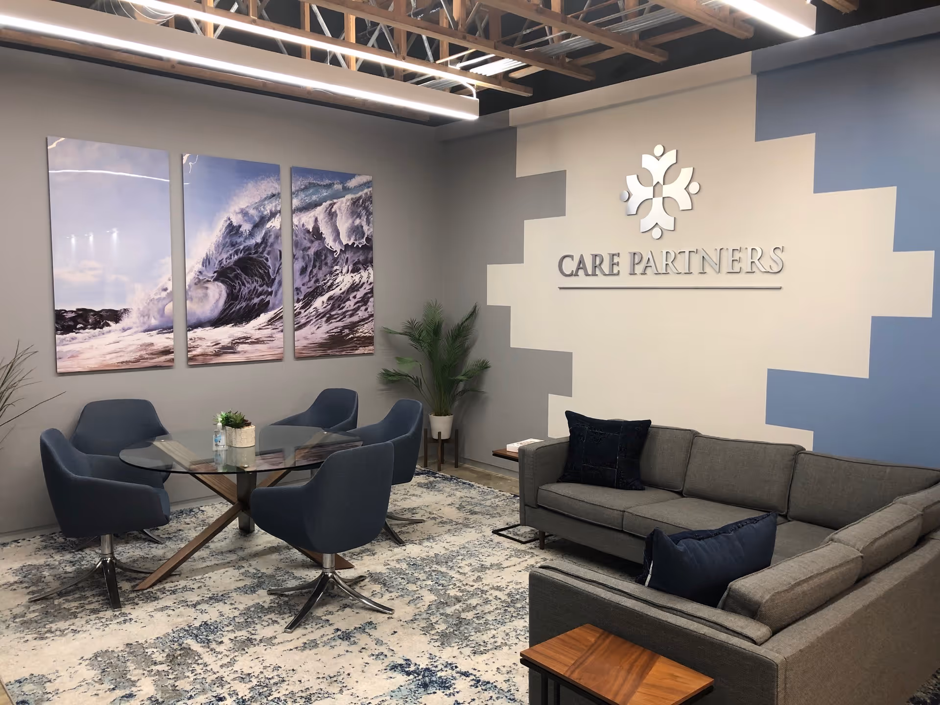 Modern reception lounge with glass table, blue chairs, gray sofa, and Care Partners logo.