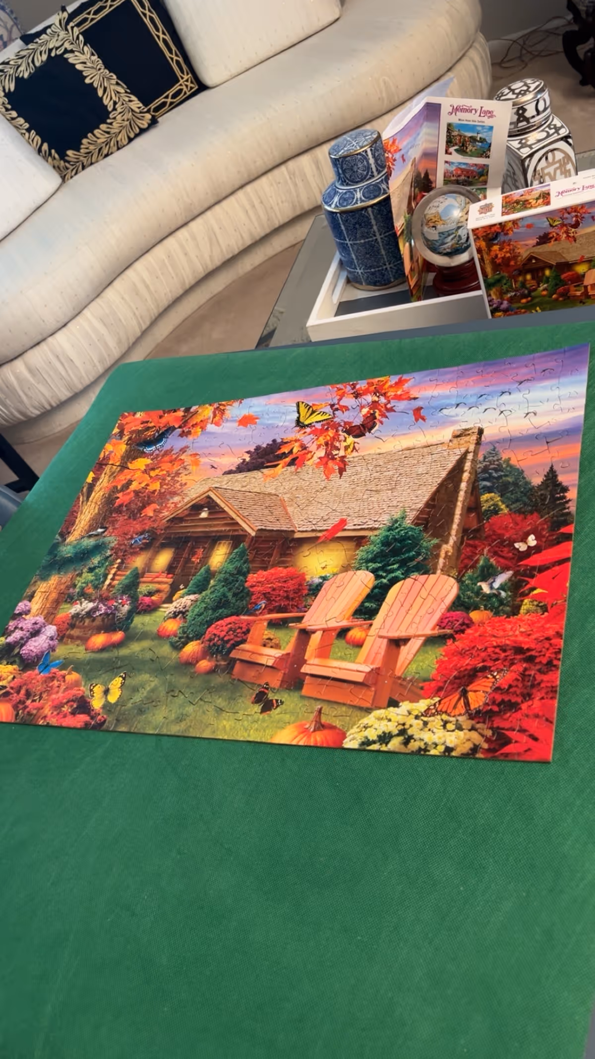 A completed jigsaw puzzle on a green table with a sofa and decorative items indoors.