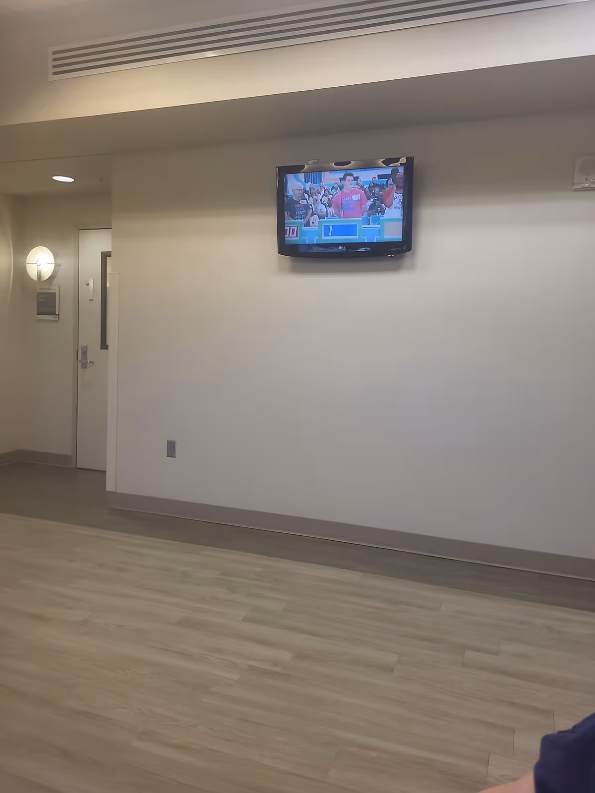 Television mounted on a light wall in a clean senior facility lobby area.