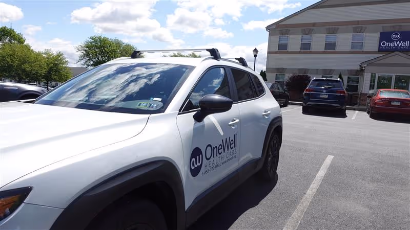 White SUV with OneWell Health Care logo parked in a lot in front of a building.