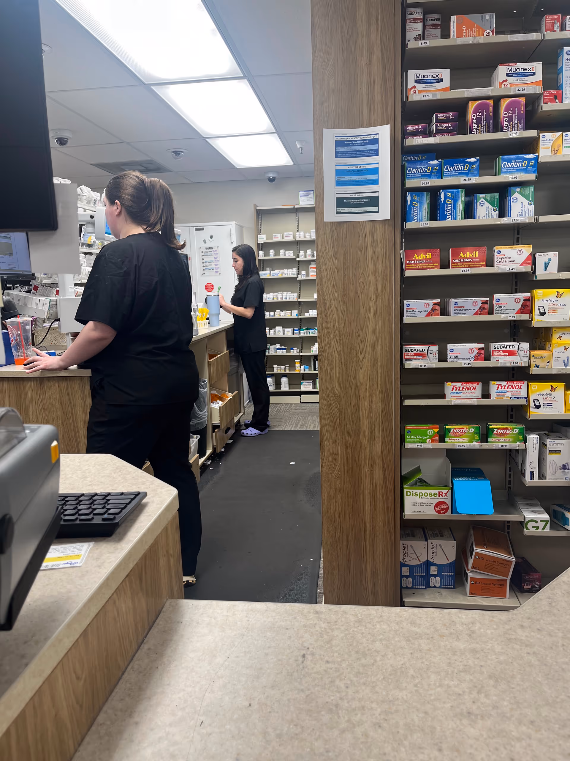 Kroger Pharmacy interior with two staff members at a counter beside medication shelves.