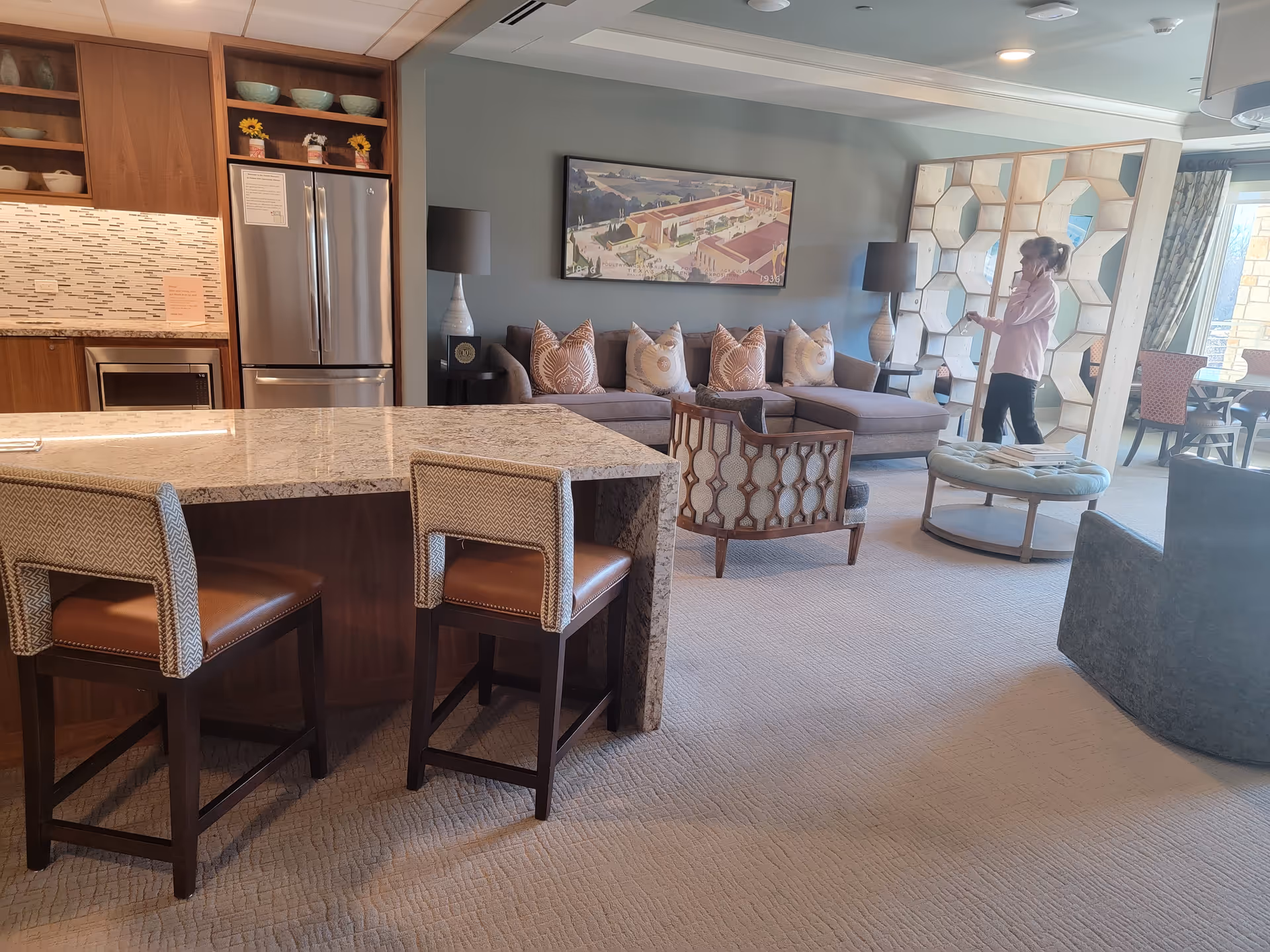 Open living area with sofa, chairs, kitchen island, and a person near wall art