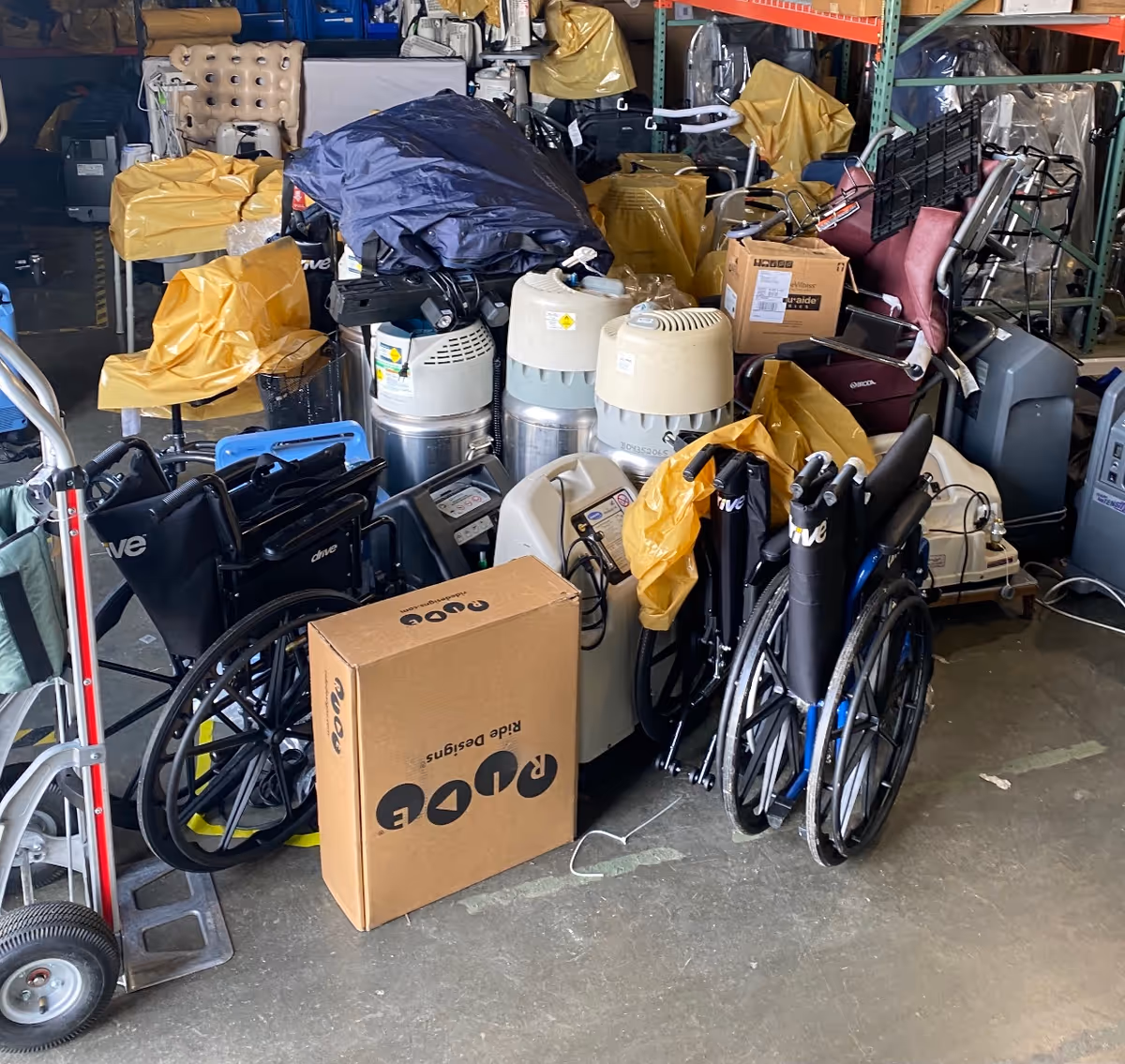 Cluttered interior storage area at Lincare with wheelchairs, oxygen tanks, boxes and covered equipment.