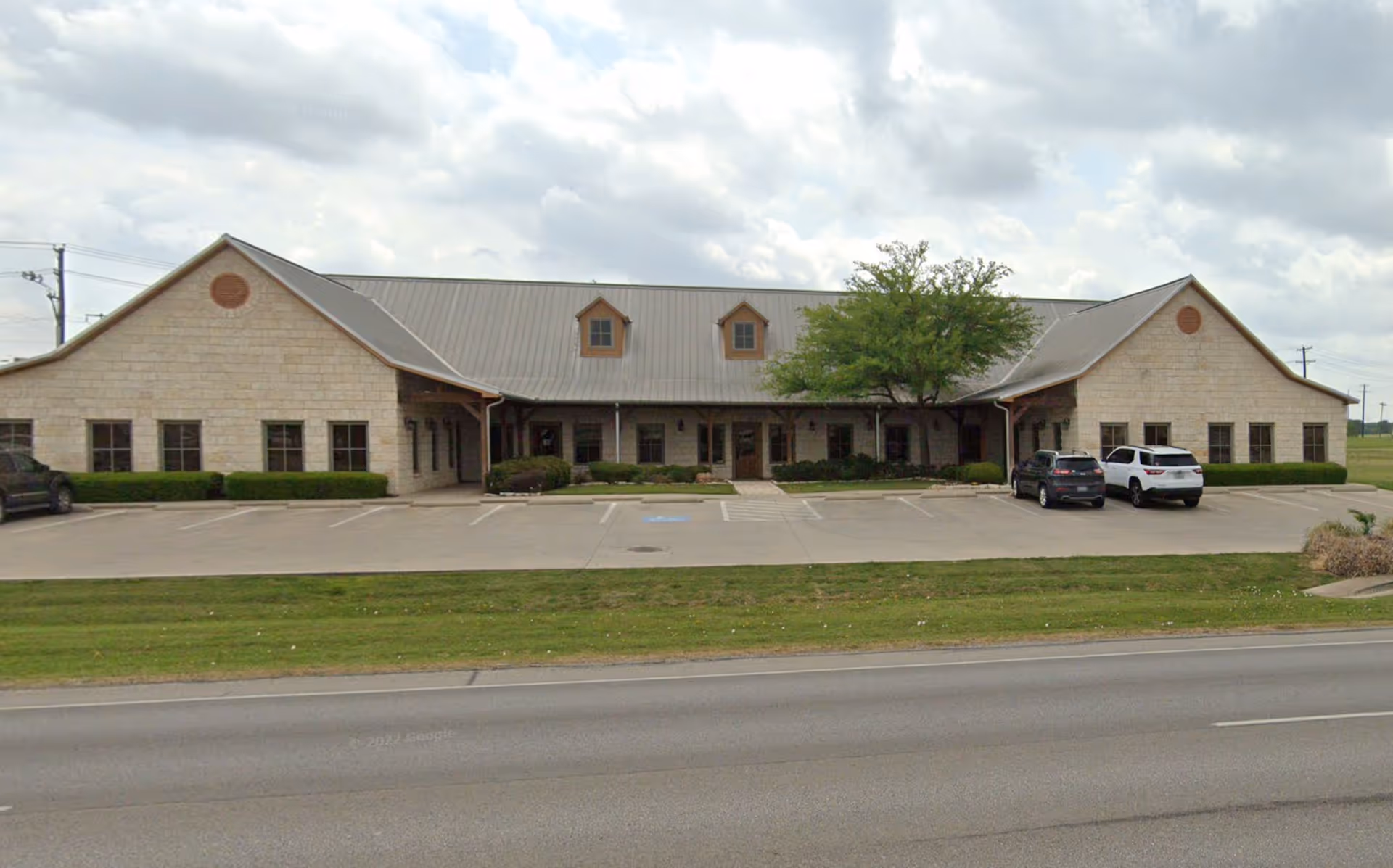 Single-story stone building with a front parking lot and a tree.