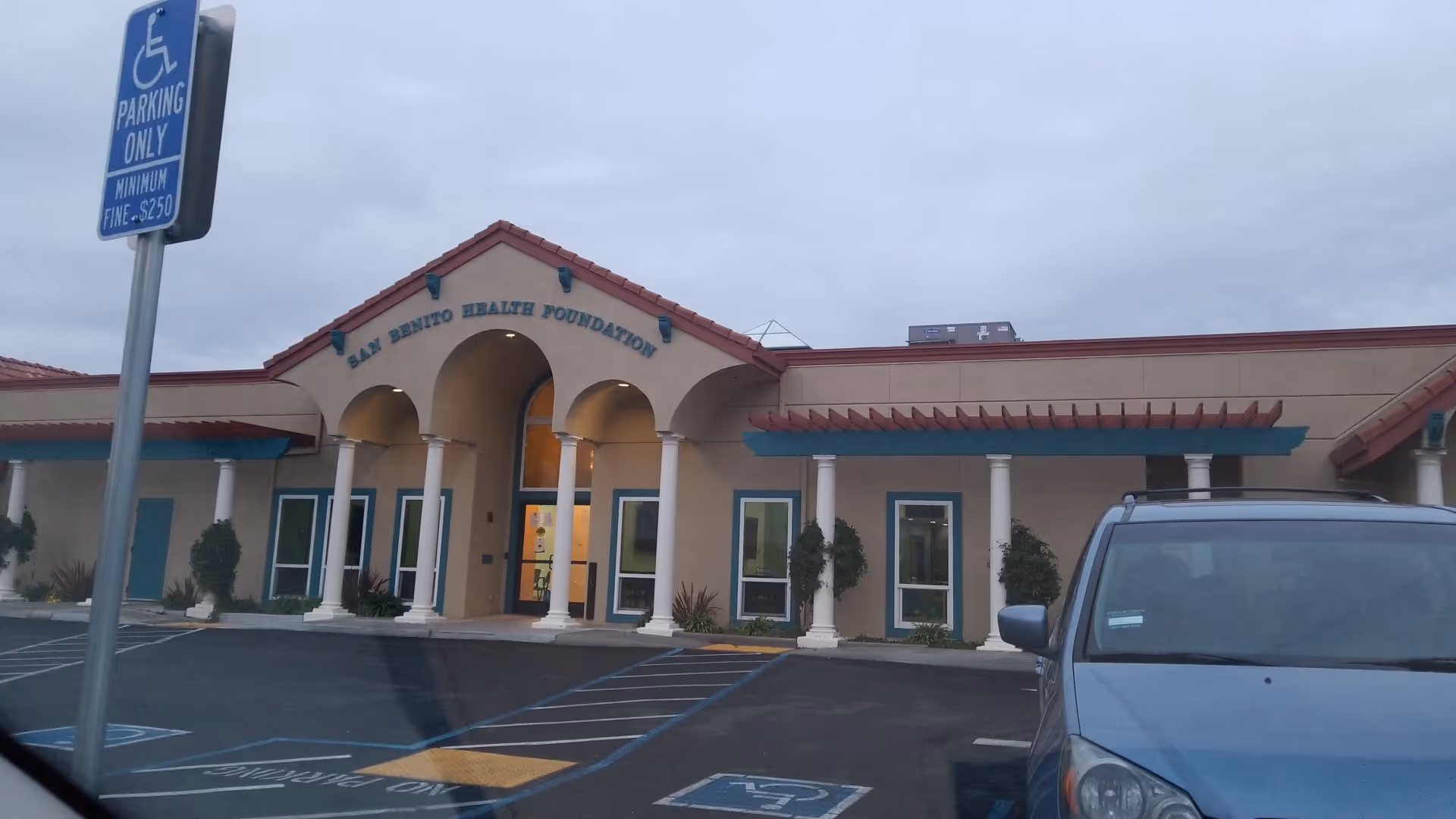 Front view of San Benito Health Foundation building with arches and a parking lot.