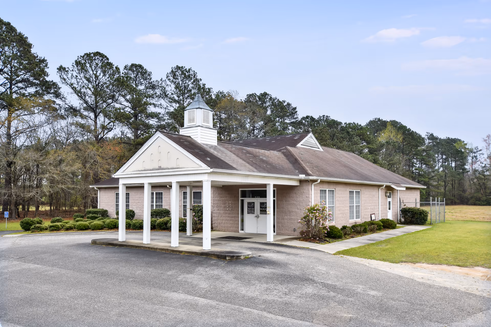 Single-story beige brick senior care building with a covered entrance and parking lot.