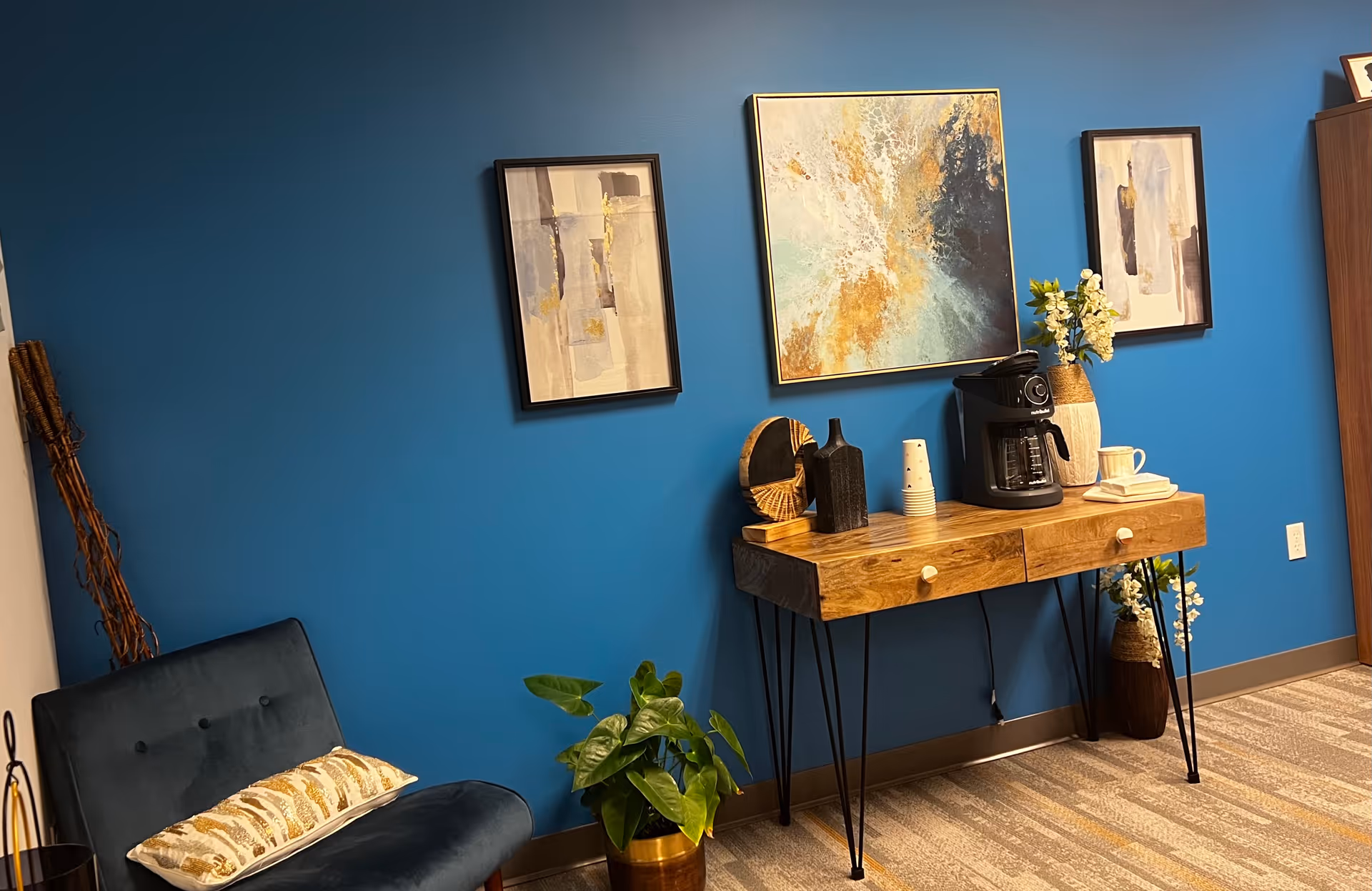 Blue-walled lounge area featuring a wooden console, coffee station, framed art, and potted plants.