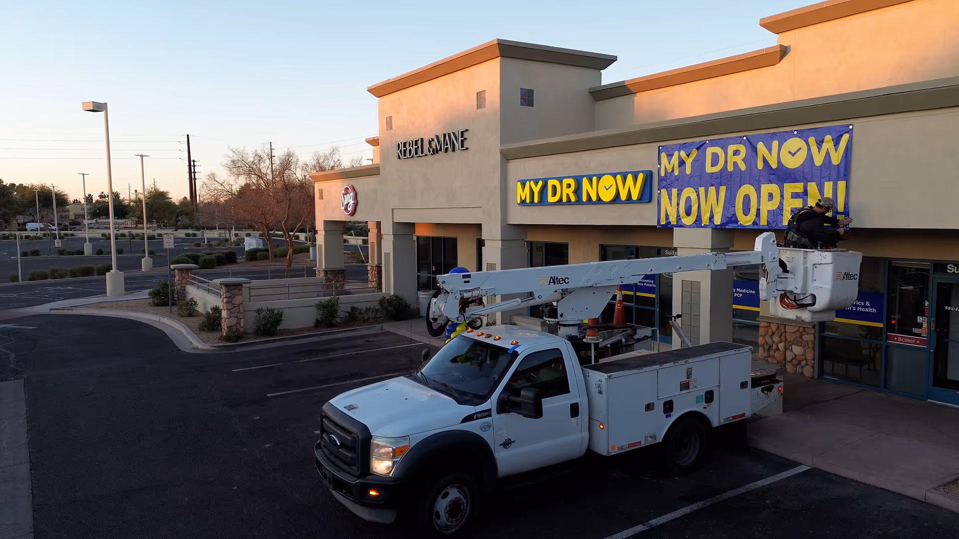 White bucket truck with elevated platform in front of MY DR NOW storefront
