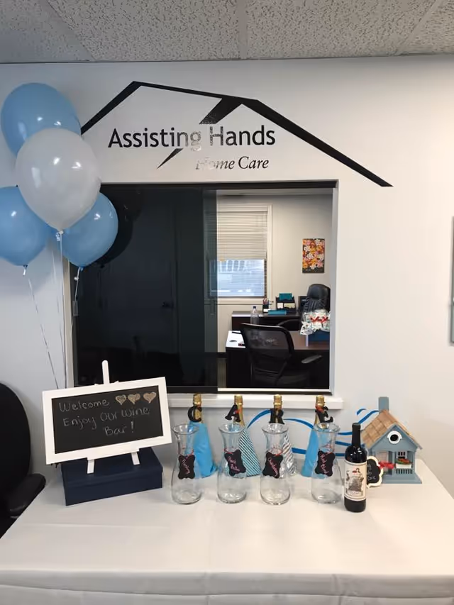 Reception area with Assisting Hands logo, balloons, and wine display.