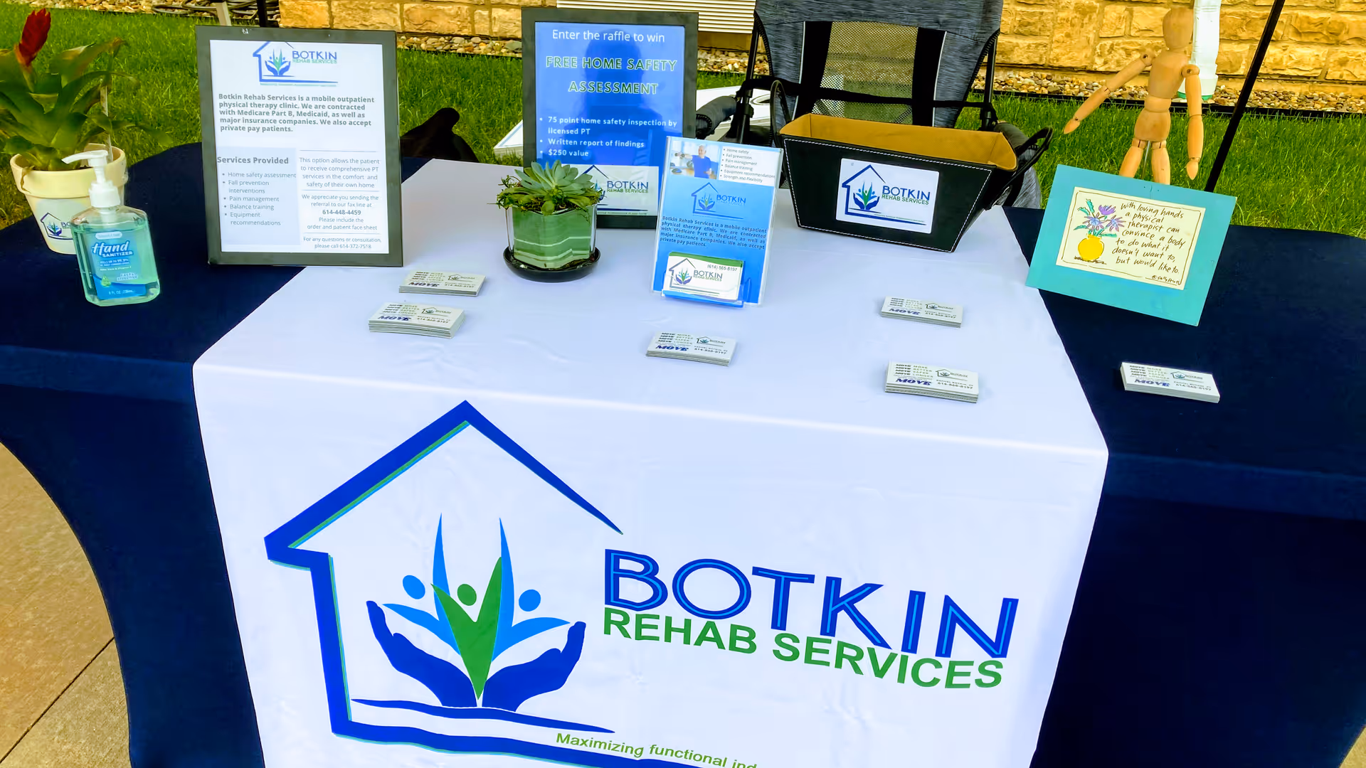 Outdoor promotional table for Botkin Rehab Services displaying brochures, signage, and a branded banner.