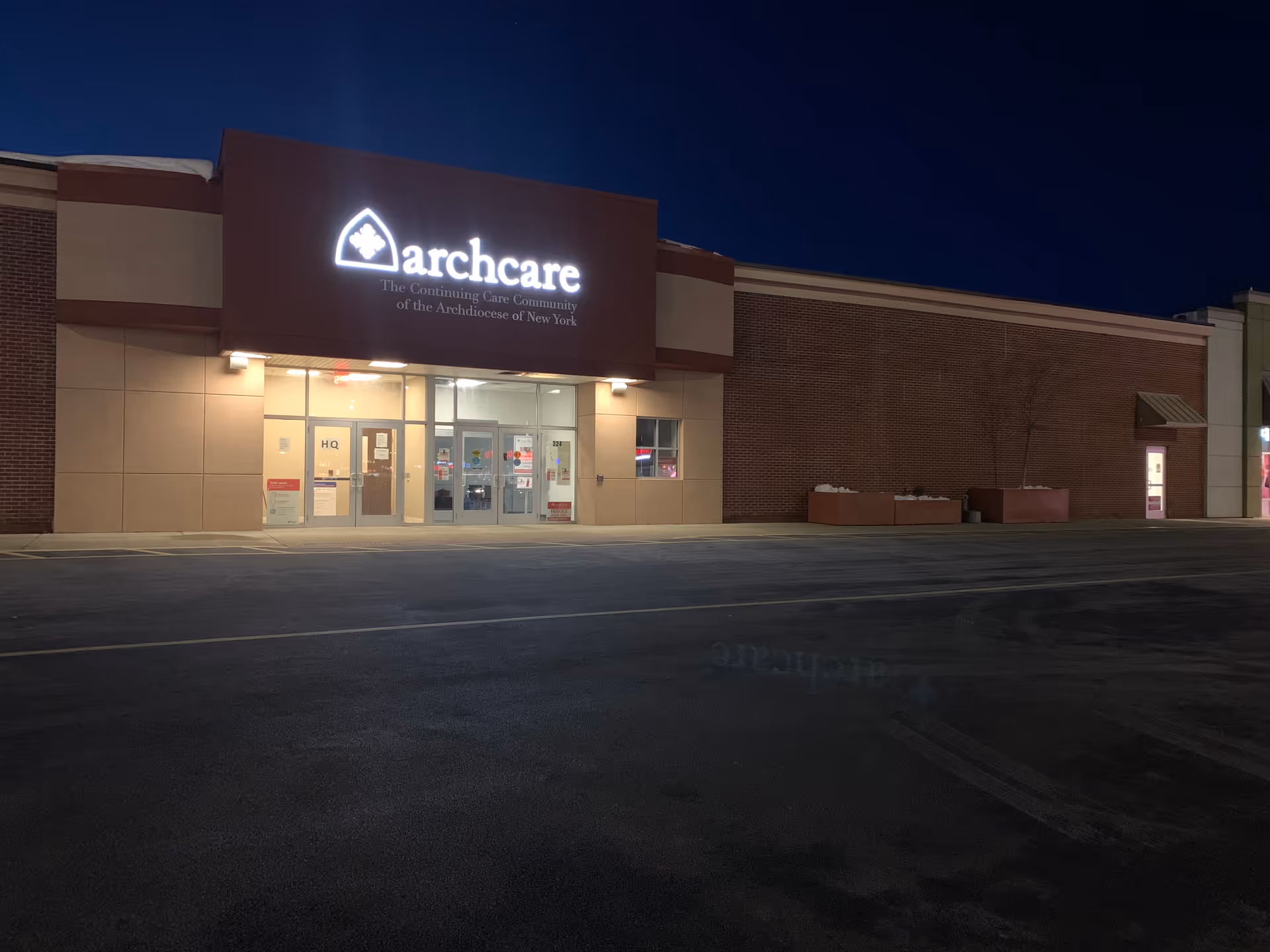 Night view of ArchCare at Home building front with illuminated sign and glass doors.