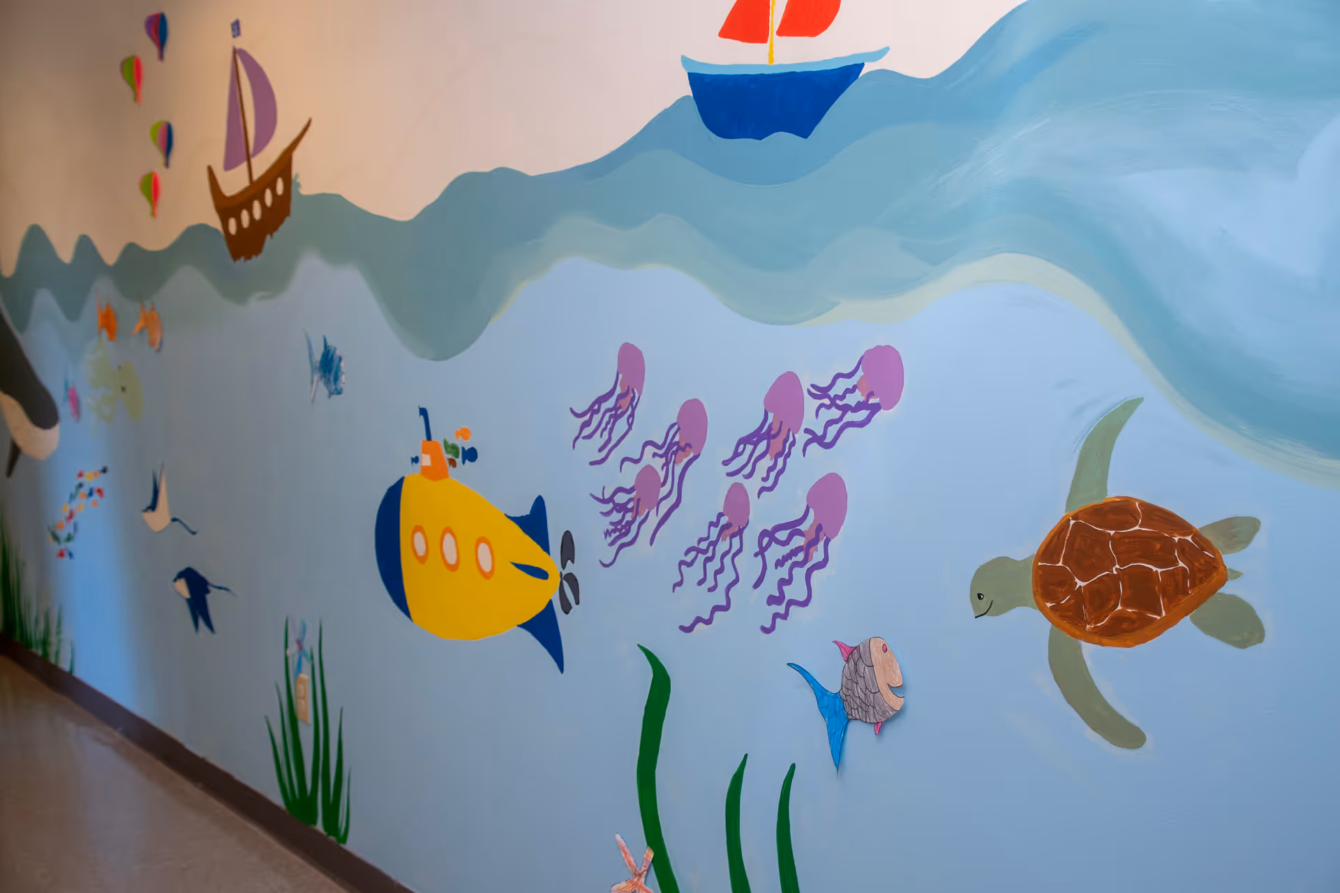 Colorful underwater mural on a hallway wall depicting fish, jellyfish, and a turtle.