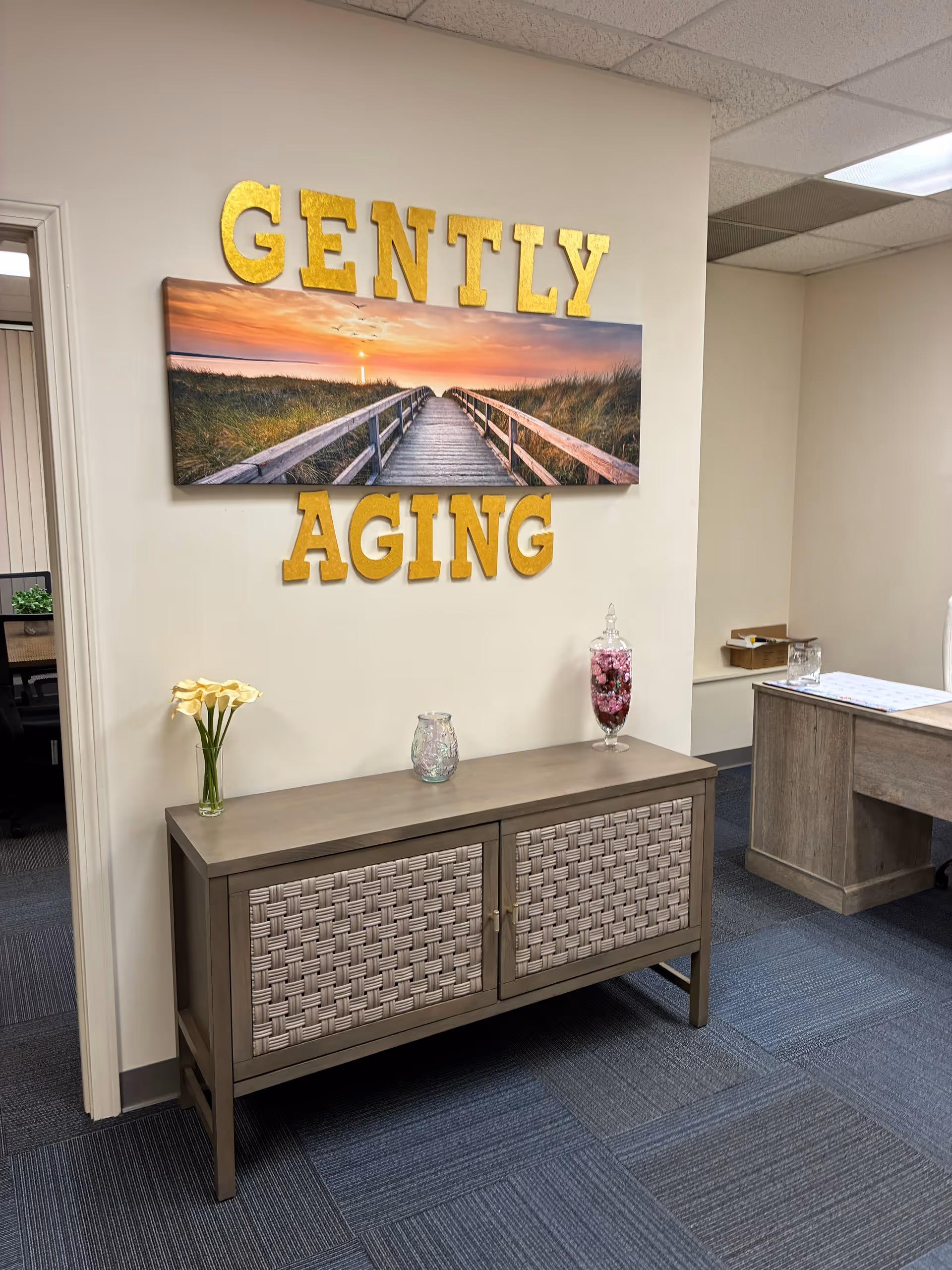Reception area with a console, 'GENTLY AGING' sign, and landscape wall art.