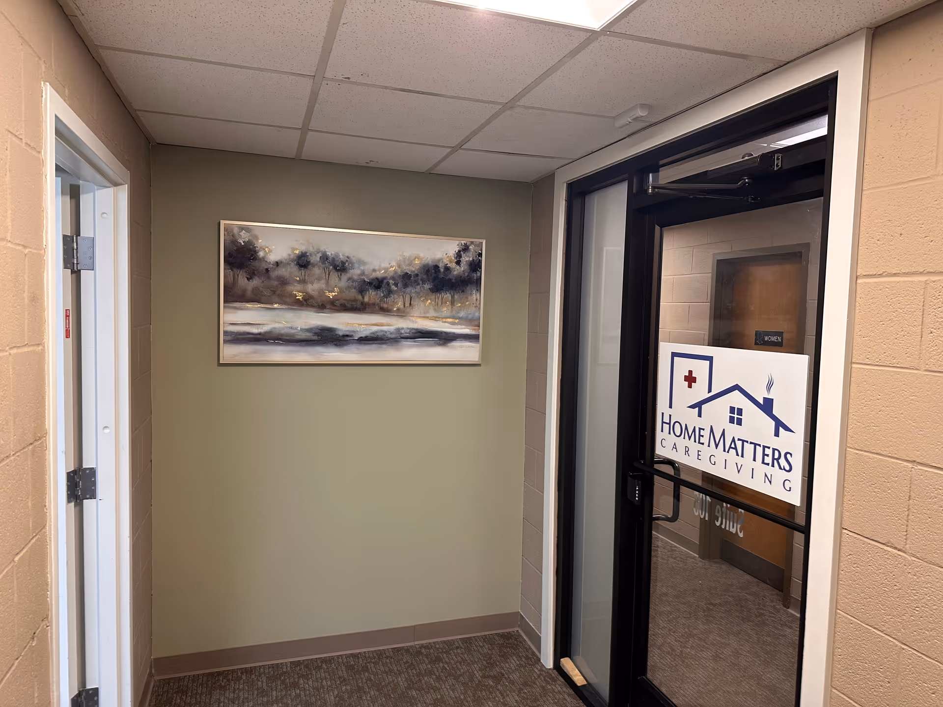 Indoor hallway with beige walls, a landscape painting, and a glass door showing Home Matters Caregiving.