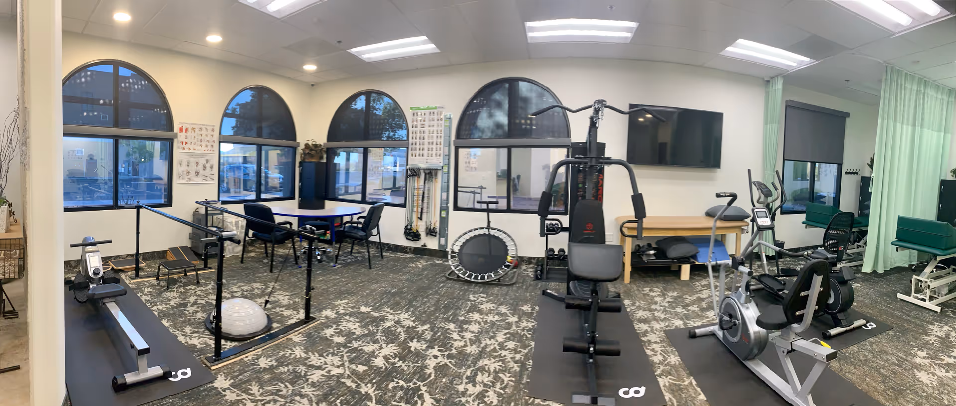 Bright rehabilitation gym inside a senior living facility featuring treadmills, bikes, weights, and balance equipment.