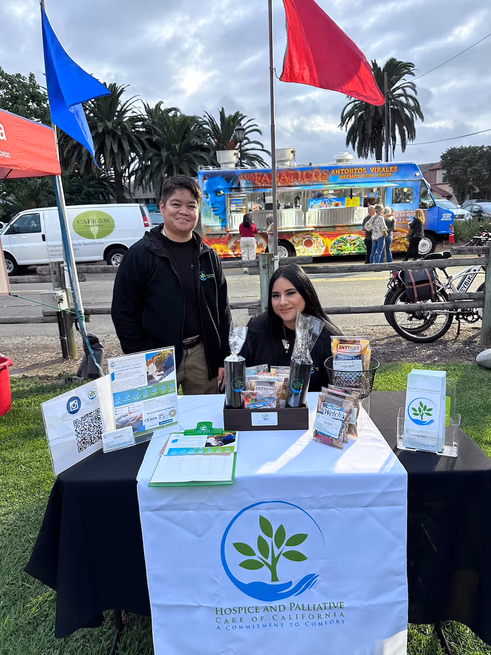 Two staff members standing beside a Hospice and Palliative Care of California table at outdoor event.