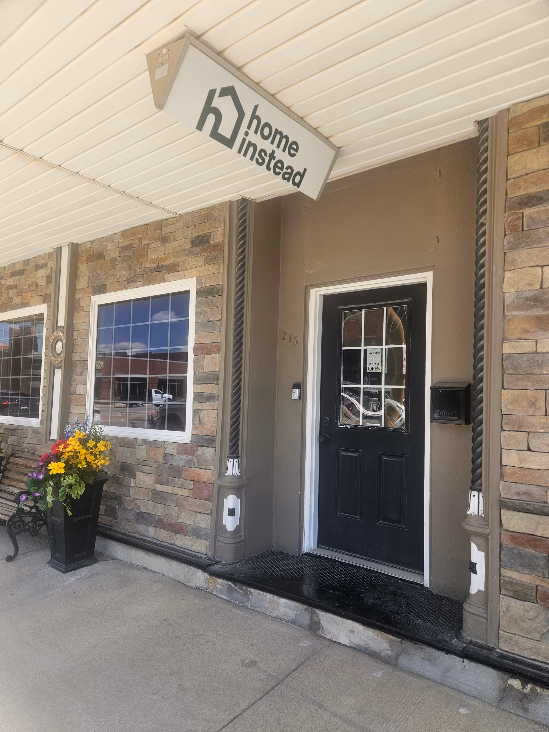 Exterior view of a Home Instead building entrance with sign and flowers.