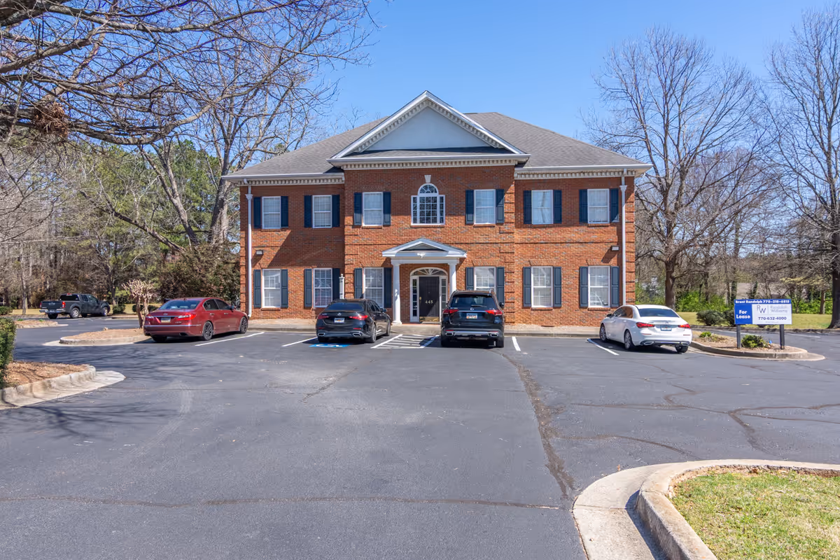 Brick two-story building with central entrance and a parking lot.