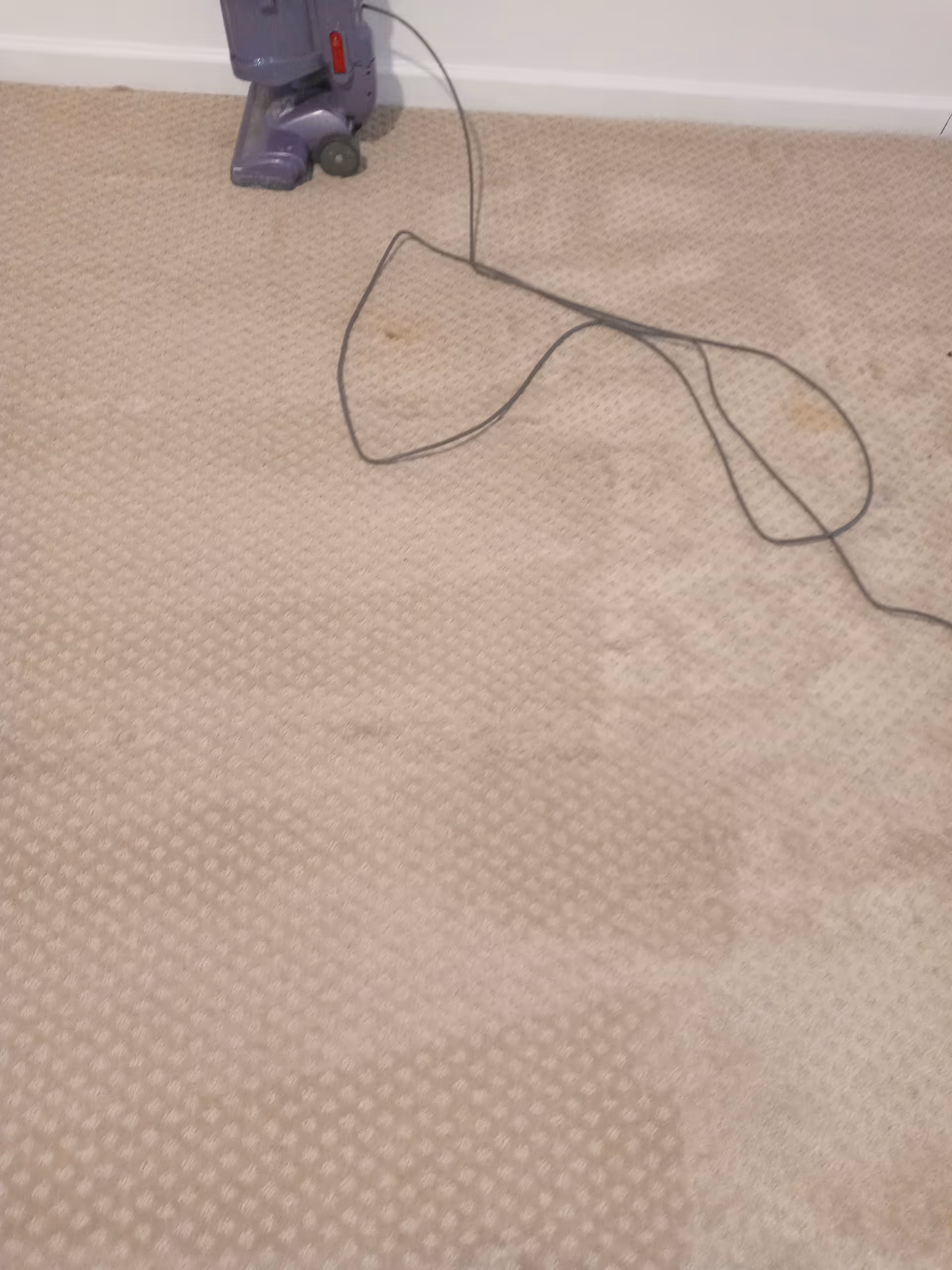A vacuum cleaner on a beige carpet with a tangled cord indoors.