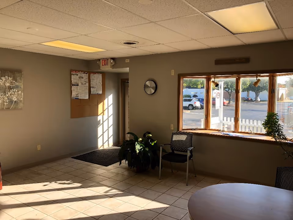 Indoor facility lobby with chairs, bulletin board, exit sign, and large window.