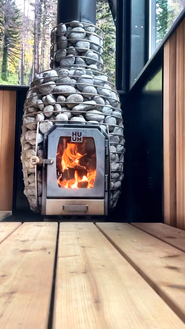 Wood-burning sauna stove surrounded by stacked stones inside a warm wood-paneled interior.