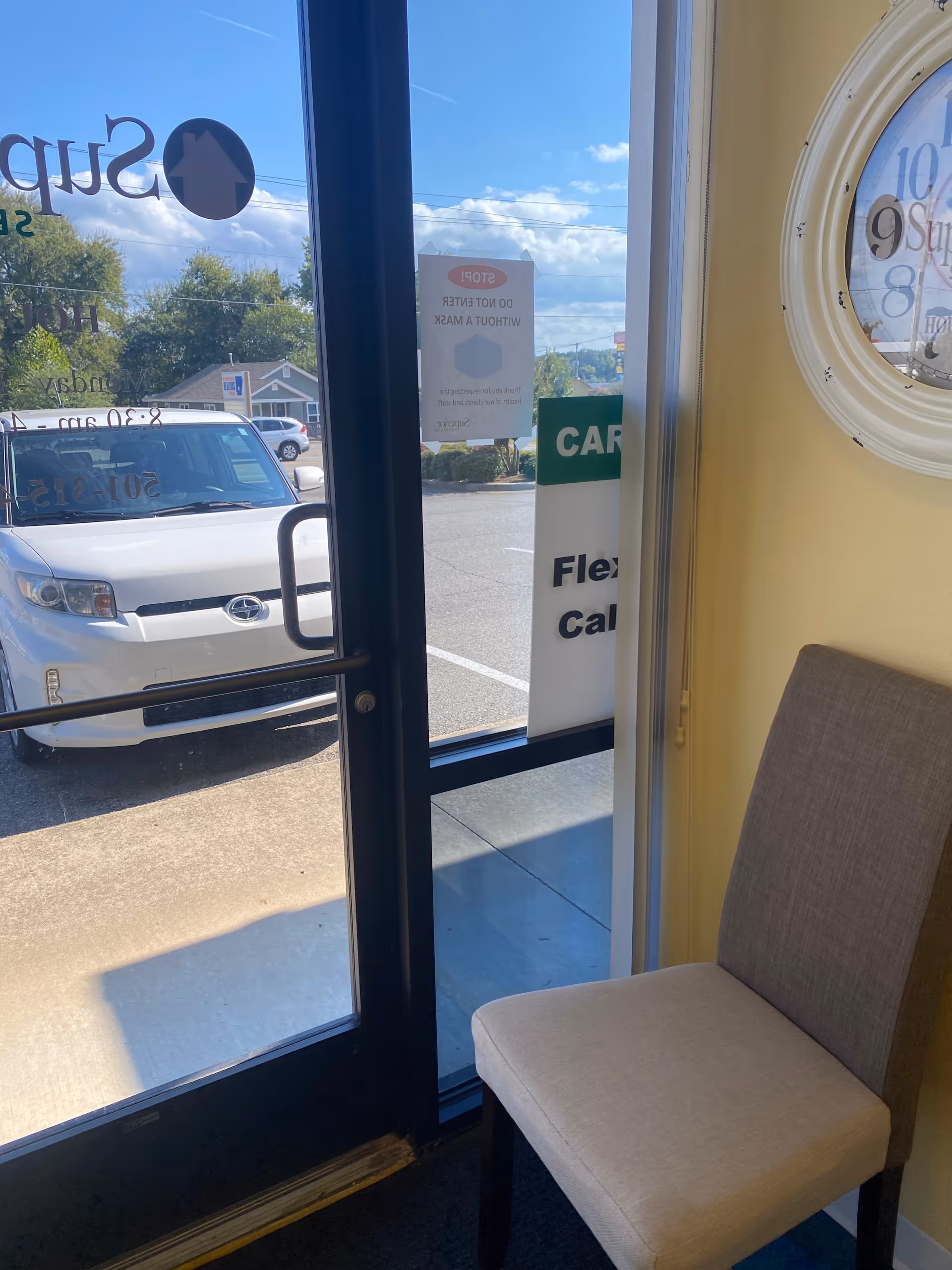 Interior entrance area with glass door, beige chair, clock, and outside view.