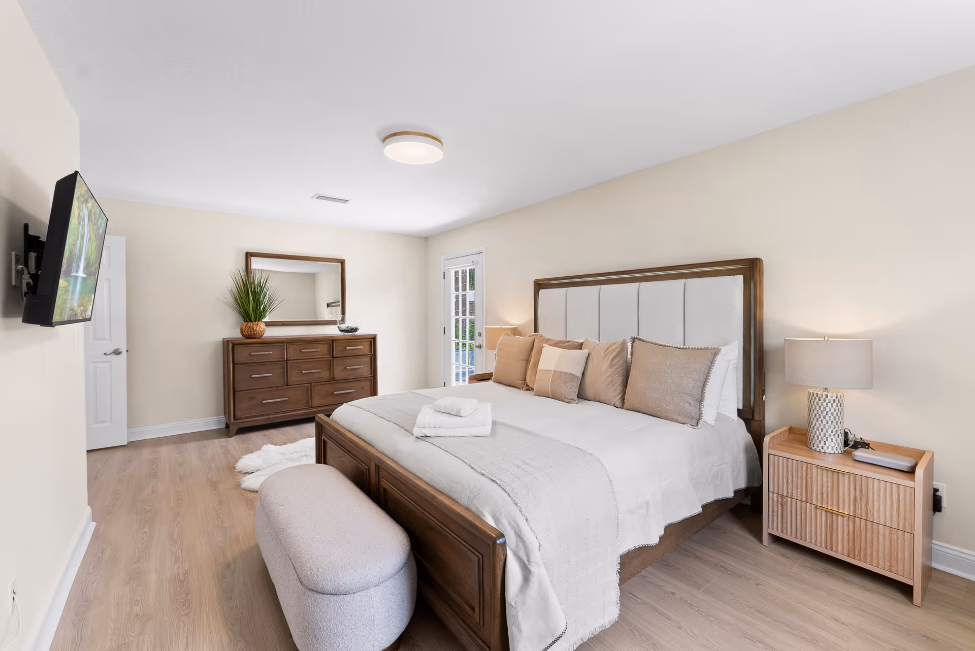 Neutral modern bedroom with a large bed, dresser, mirror, and wall-mounted television.
