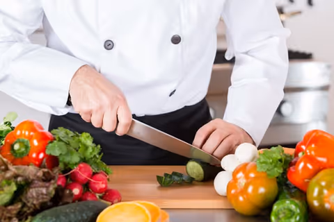 Chef in a white coat chops vegetables on a cutting board in a kitchen.