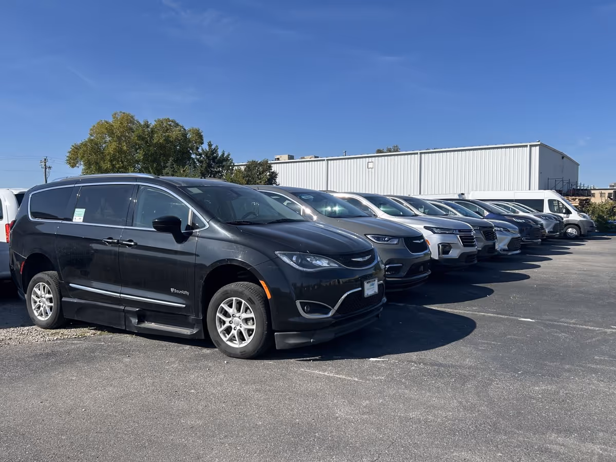 Row of MobilityWorks vans parked in a lot beside a metal industrial building.