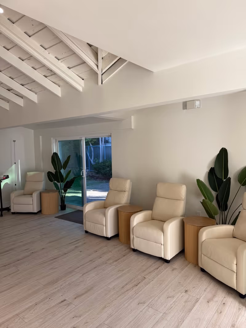 Bright modern lounge with beige recliners, plants, and a sliding glass door.