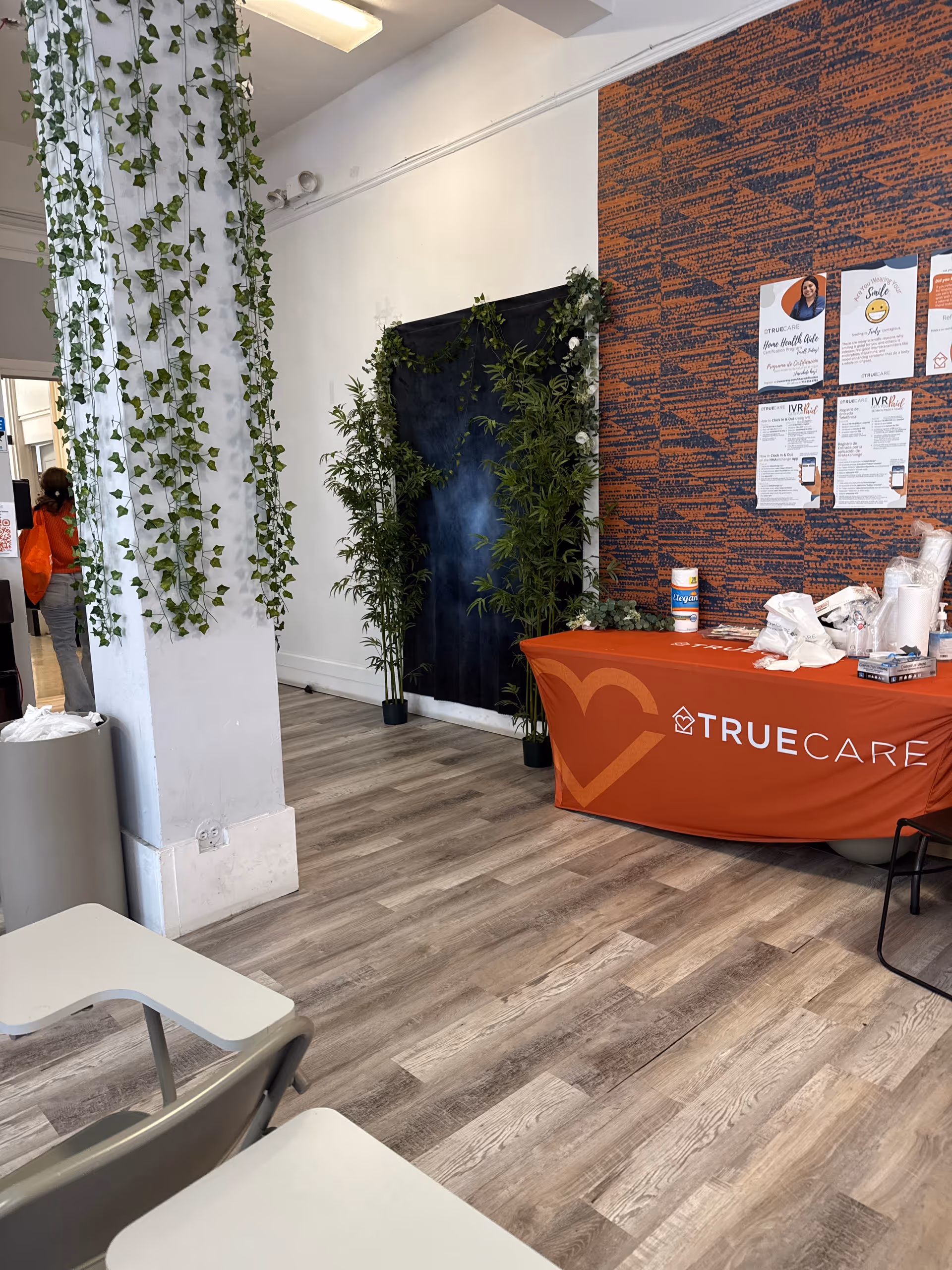 Inside a TrueCare reception area with an orange banner and hanging greenery