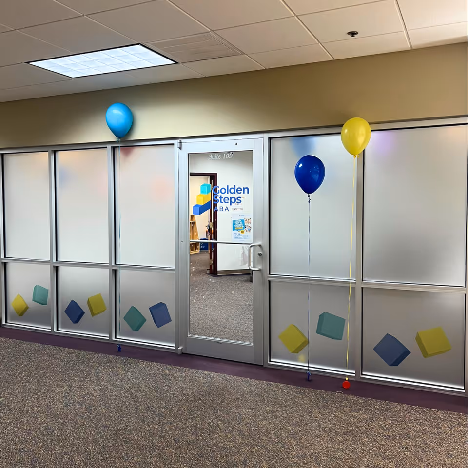 Frosted glass hallway with door labeled Golden Steps ABA and colorful balloon decorations.