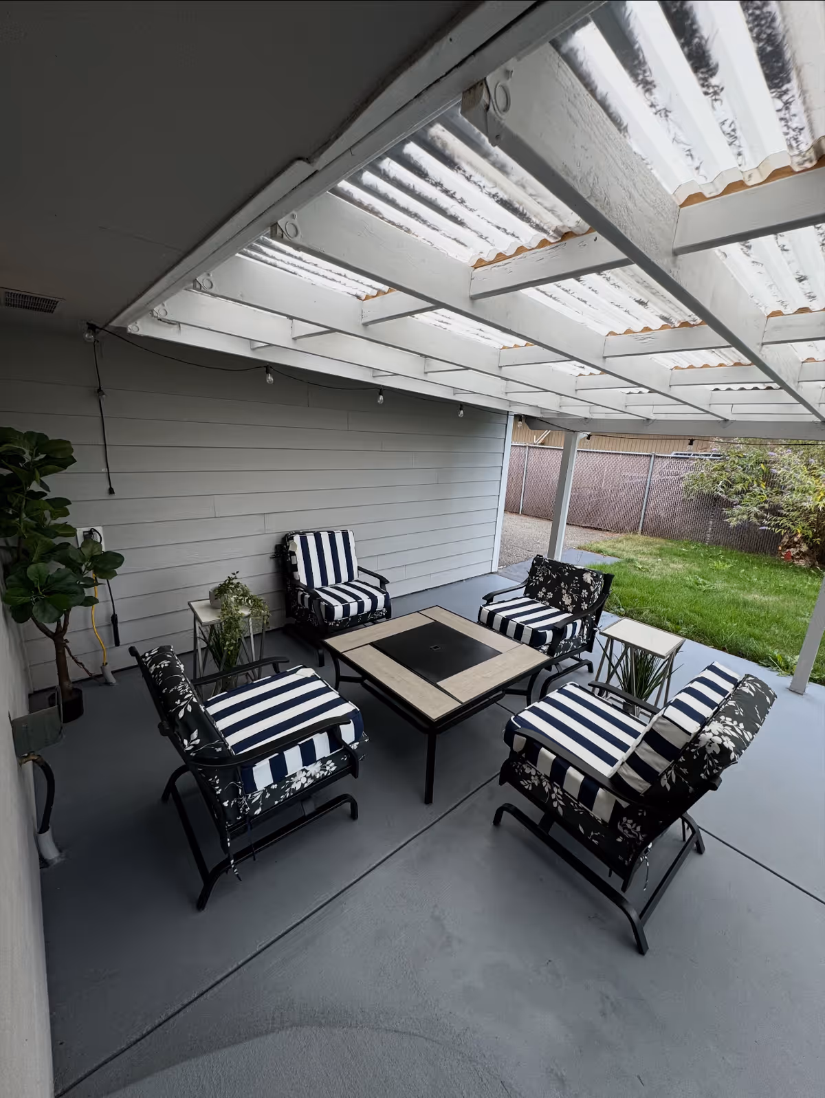Covered outdoor patio with striped cushioned seating around a central fire pit table.