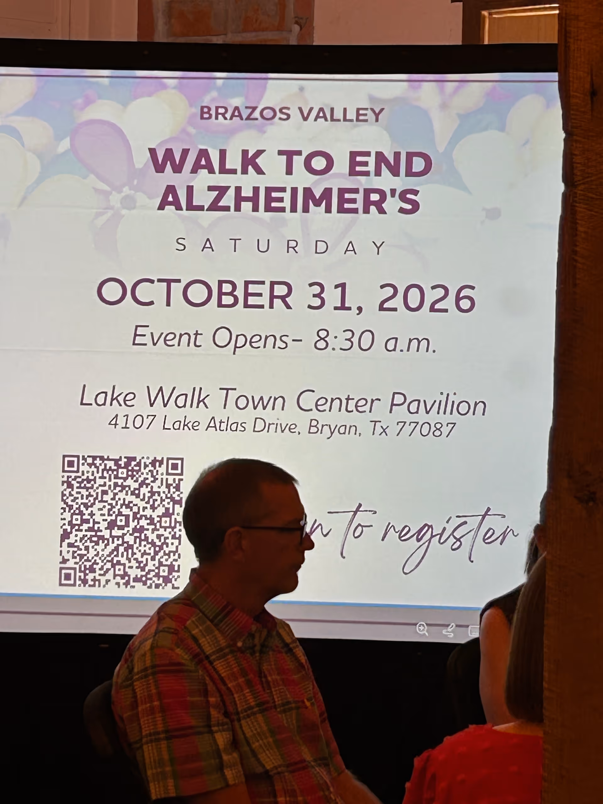 Indoor event scene with a large projection screen displaying Walk to End Alzheimer's information.