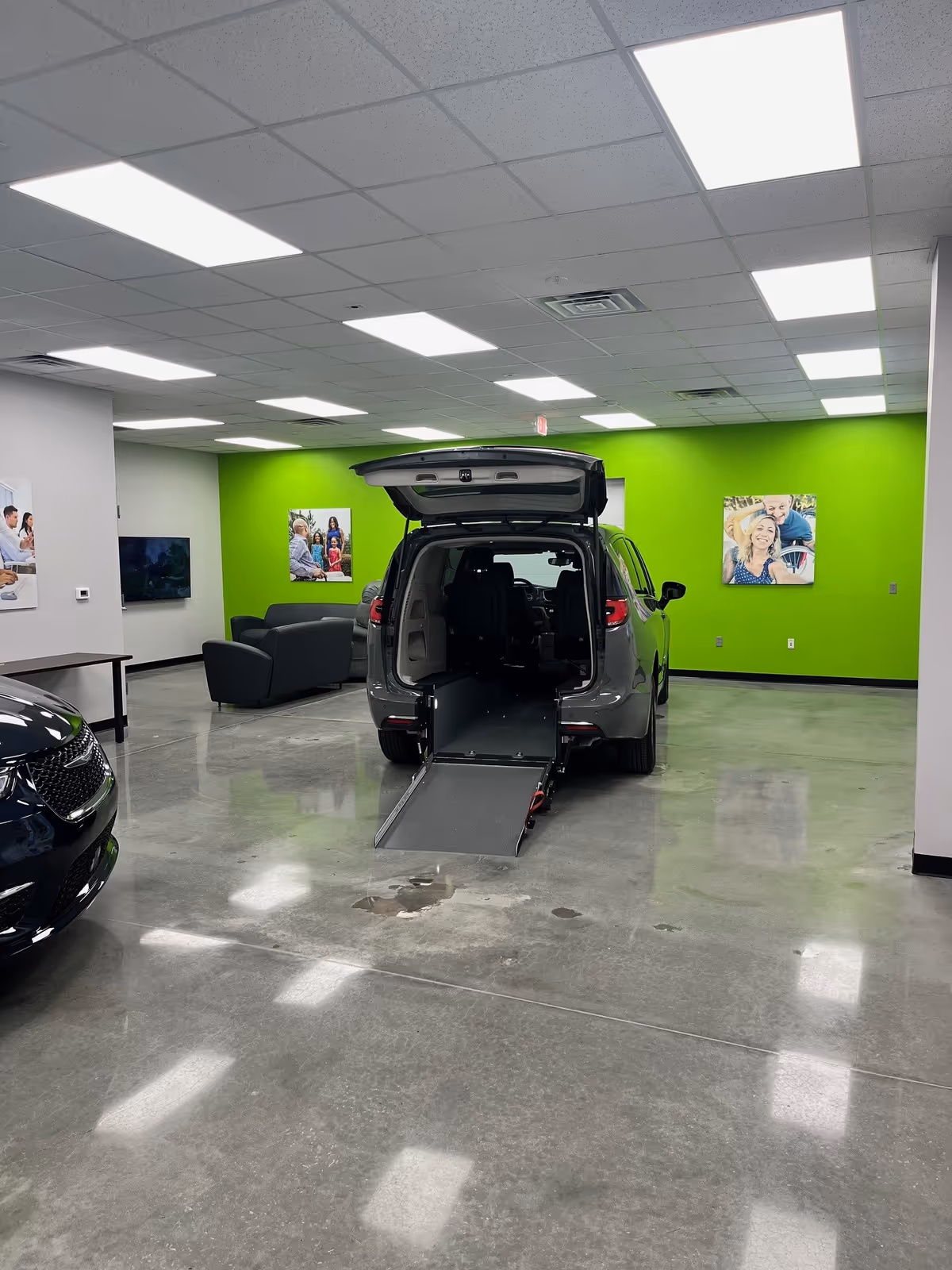 Indoor showroom with a wheelchair-accessible van and extended ramp against a lime-green wall.