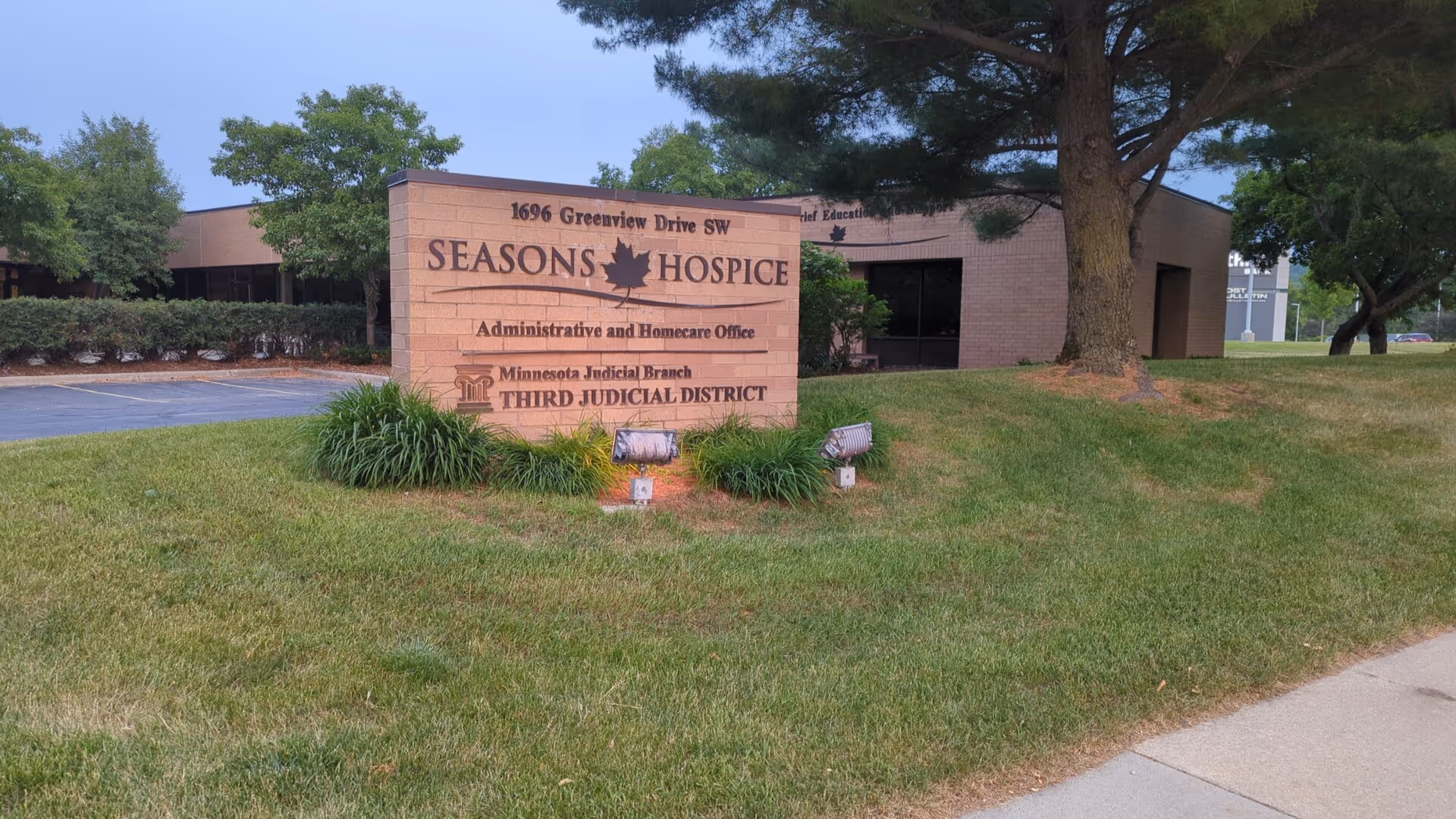 Exterior view of Seasons Hospice facility with brick sign and landscaping.
